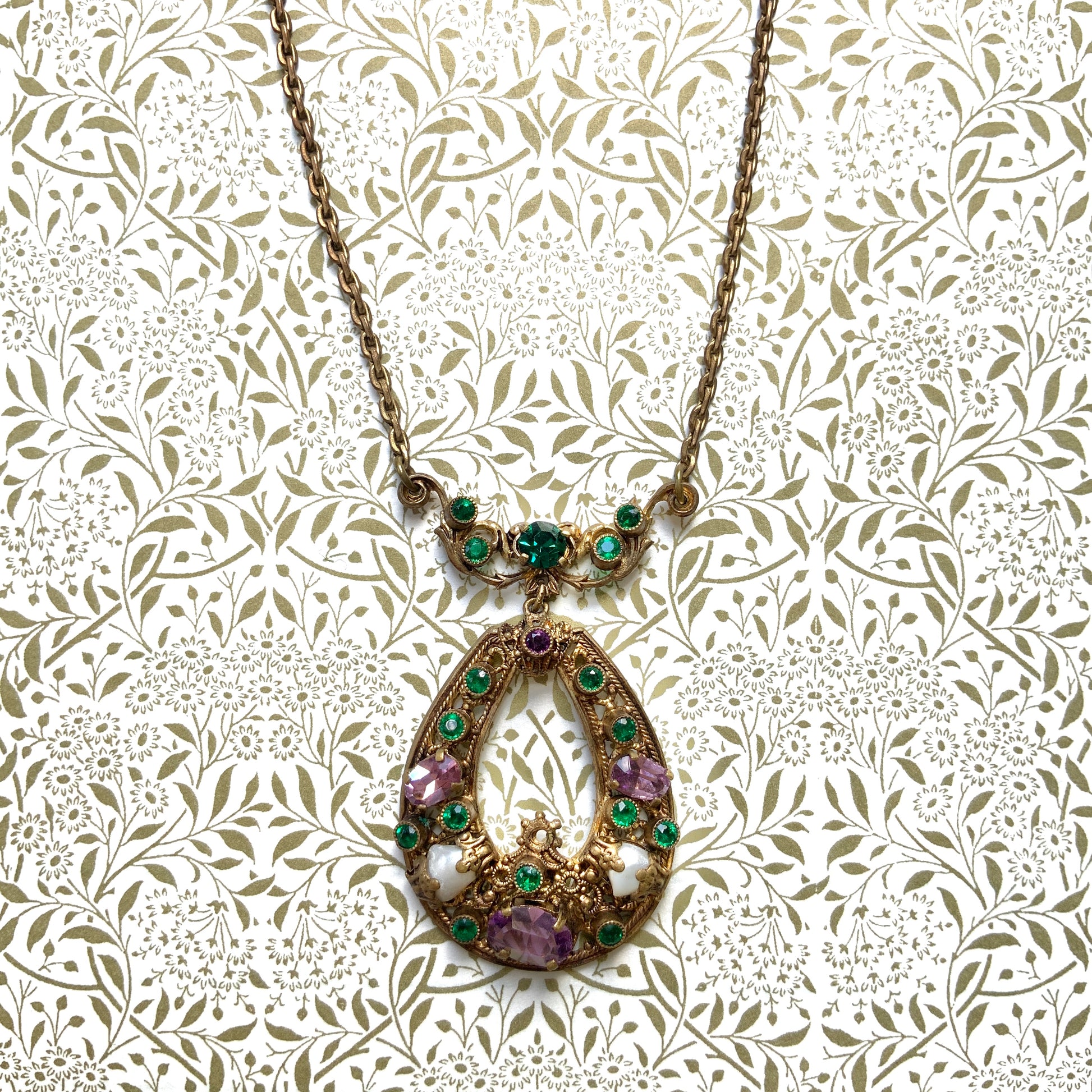This necklace features a beautiful gold-tone teardrop hoop filigree, adorned with green, purple, and white stones in the colours of the suffragette movement.  美しいゴールドトーンのティアドロップフープ のフィリグリーに、緑、紫、白のサフラジェットカラーのストーンがついたネックレス。