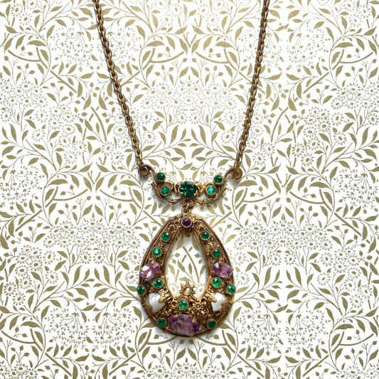 This necklace features a beautiful gold-tone teardrop hoop filigree, adorned with green, purple, and white stones in the colours of the suffragette movement.  美しいゴールドトーンのティアドロップフープ のフィリグリーに、緑、紫、白のサフラジェットカラーのストーンがついたネックレス。