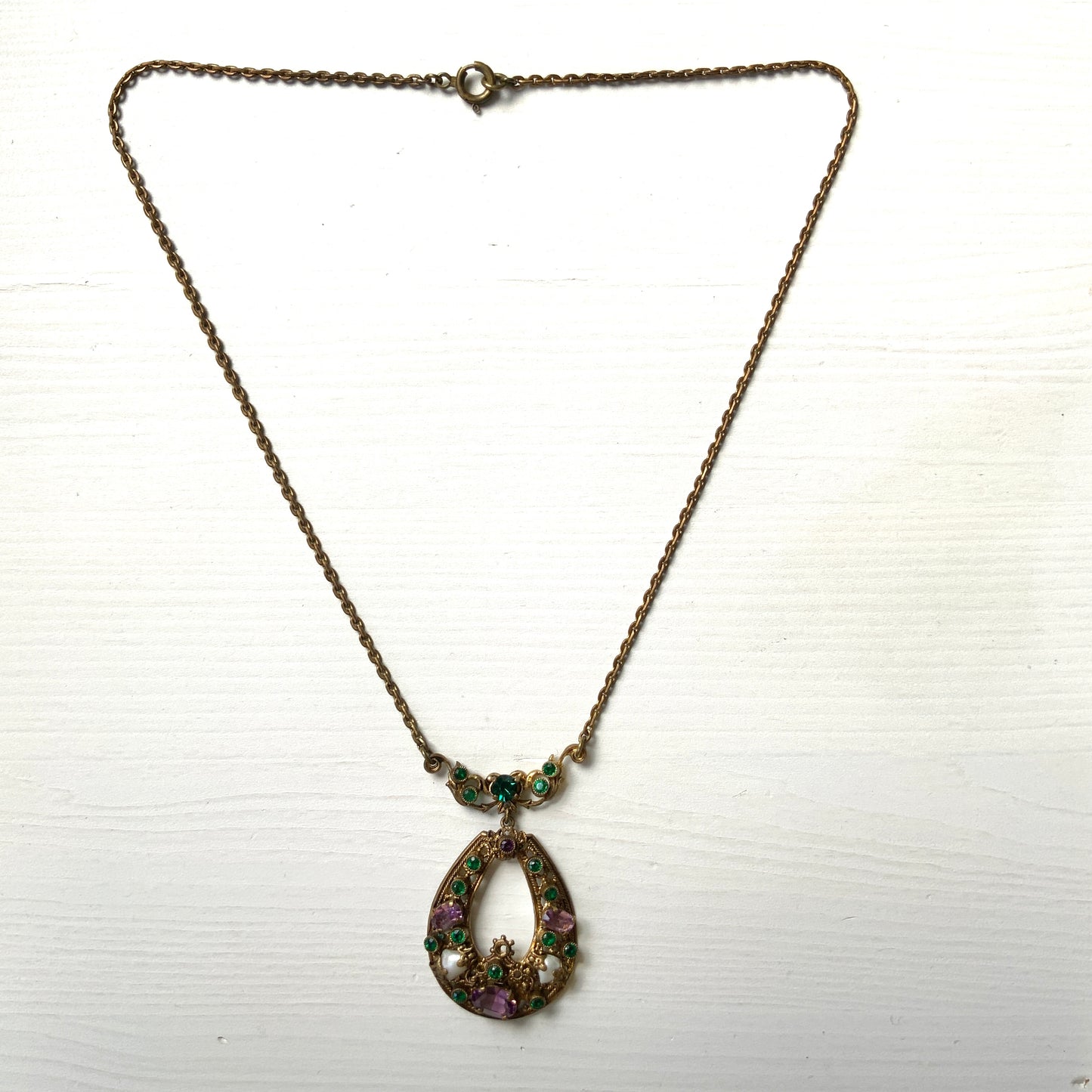 This necklace features a beautiful gold-tone teardrop hoop filigree, adorned with green, purple, and white stones in the colours of the suffragette movement. 美しいゴールドトーンのティアドロップフープ のフィリグリーに、緑、紫、白のサフラジェットカラーのストーンがついたネックレス。