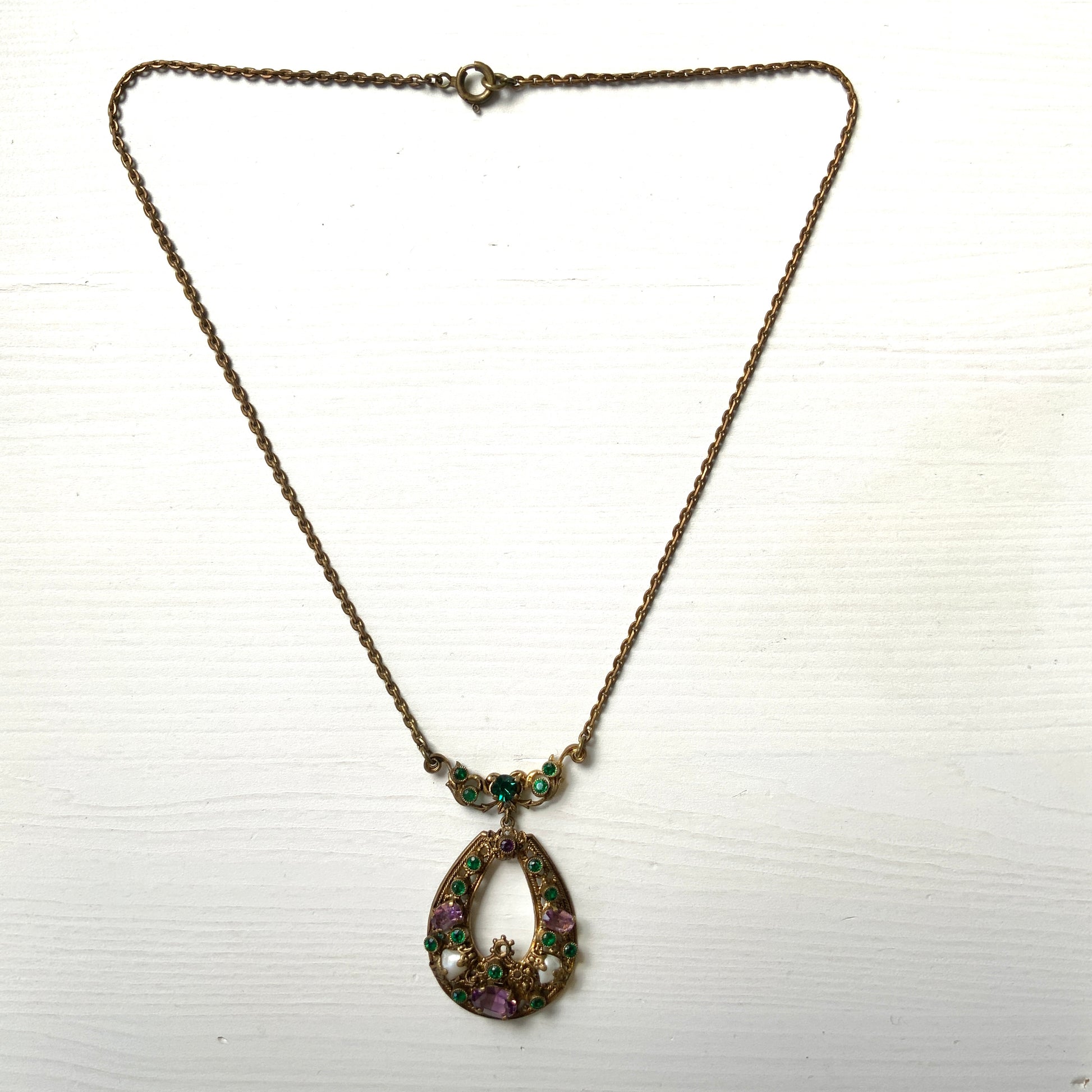This necklace features a beautiful gold-tone teardrop hoop filigree, adorned with green, purple, and white stones in the colours of the suffragette movement.  美しいゴールドトーンのティアドロップフープ のフィリグリーに、緑、紫、白のサフラジェットカラーのストーンがついたネックレス。
