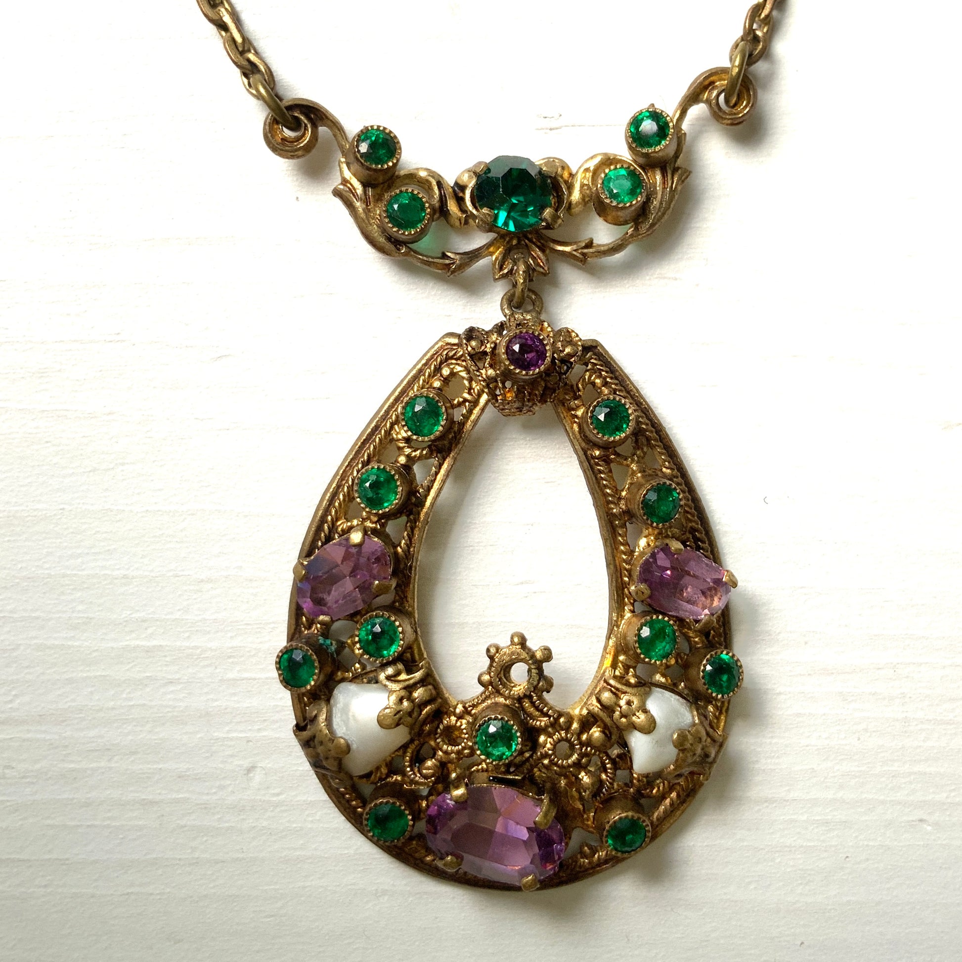 This necklace features a beautiful gold-tone teardrop hoop filigree, adorned with green, purple, and white stones in the colours of the suffragette movement.  美しいゴールドトーンのティアドロップフープ のフィリグリーに、緑、紫、白のサフラジェットカラーのストーンがついたネックレス。