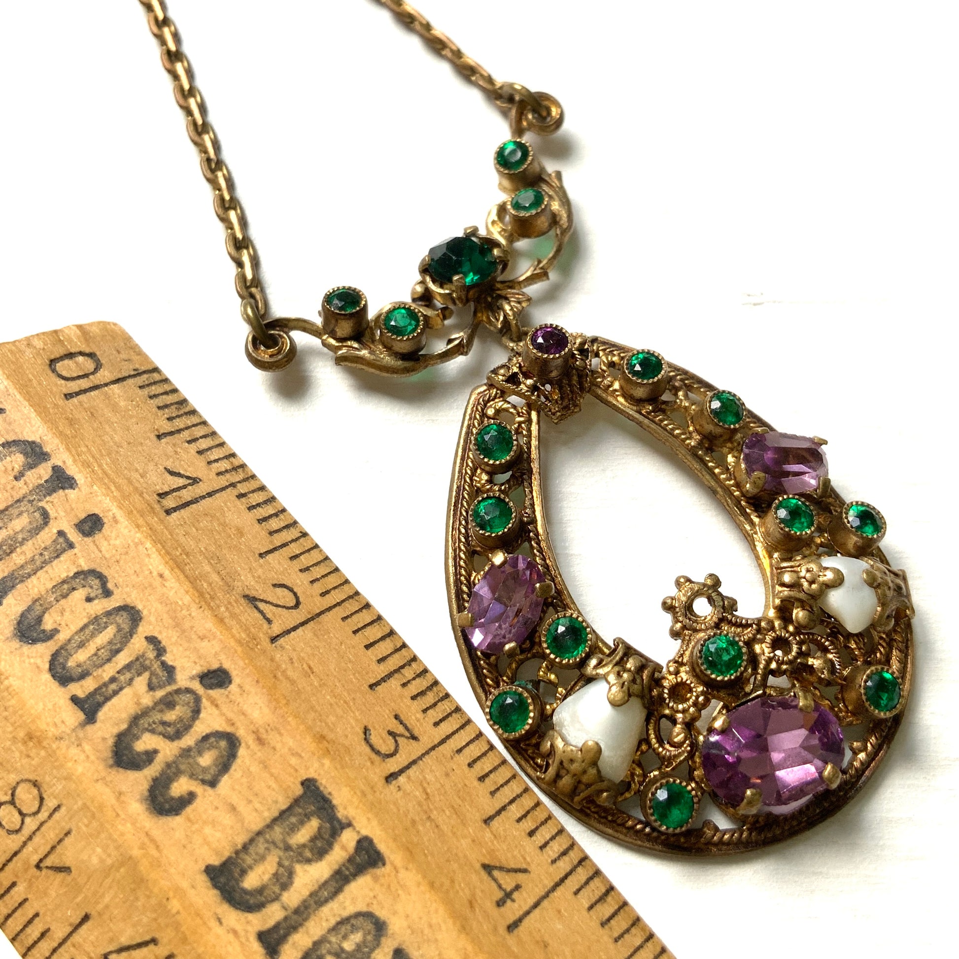 This necklace features a beautiful gold-tone teardrop hoop filigree, adorned with green, purple, and white stones in the colours of the suffragette movement.  美しいゴールドトーンのティアドロップフープ のフィリグリーに、緑、紫、白のサフラジェットカラーのストーンがついたネックレス。