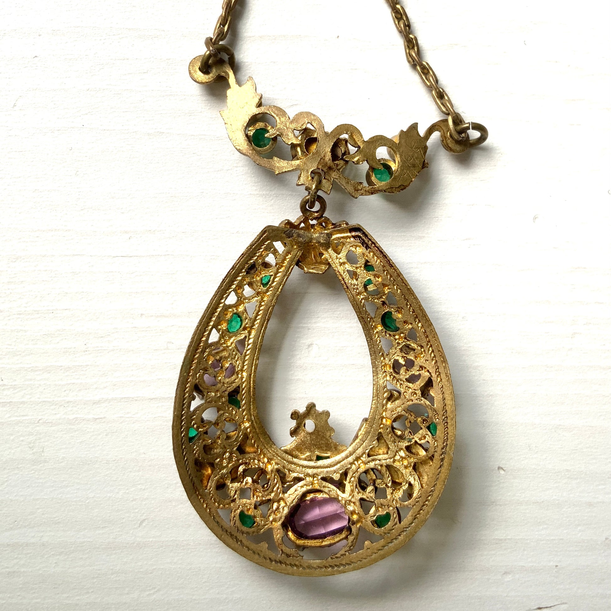 This necklace features a beautiful gold-tone teardrop hoop filigree, adorned with green, purple, and white stones in the colours of the suffragette movement.  美しいゴールドトーンのティアドロップフープ のフィリグリーに、緑、紫、白のサフラジェットカラーのストーンがついたネックレス。
