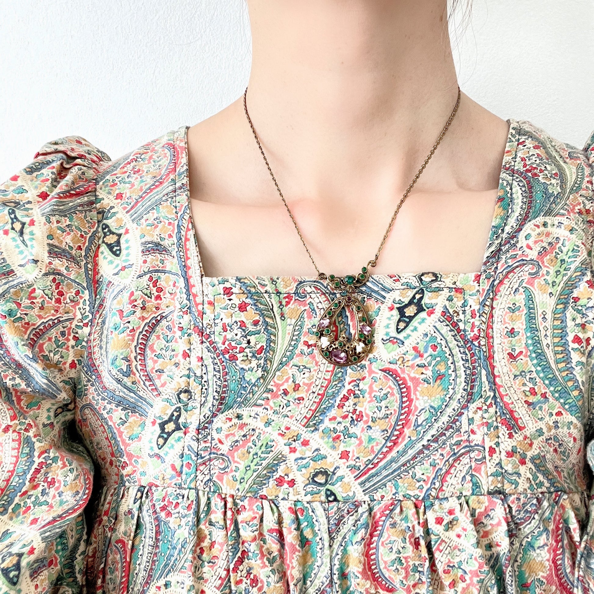 This necklace features a beautiful gold-tone teardrop hoop filigree, adorned with green, purple, and white stones in the colours of the suffragette movement.  美しいゴールドトーンのティアドロップフープ のフィリグリーに、緑、紫、白のサフラジェットカラーのストーンがついたネックレス。