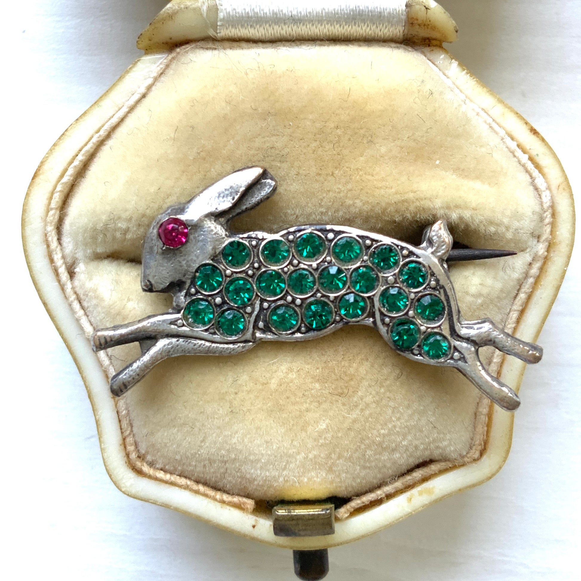 This silver brooch features a rabbit with green rhinestones adorning its body. グリーンのラインストーンをボディに纏ったうさぎのシルバーブローチ。