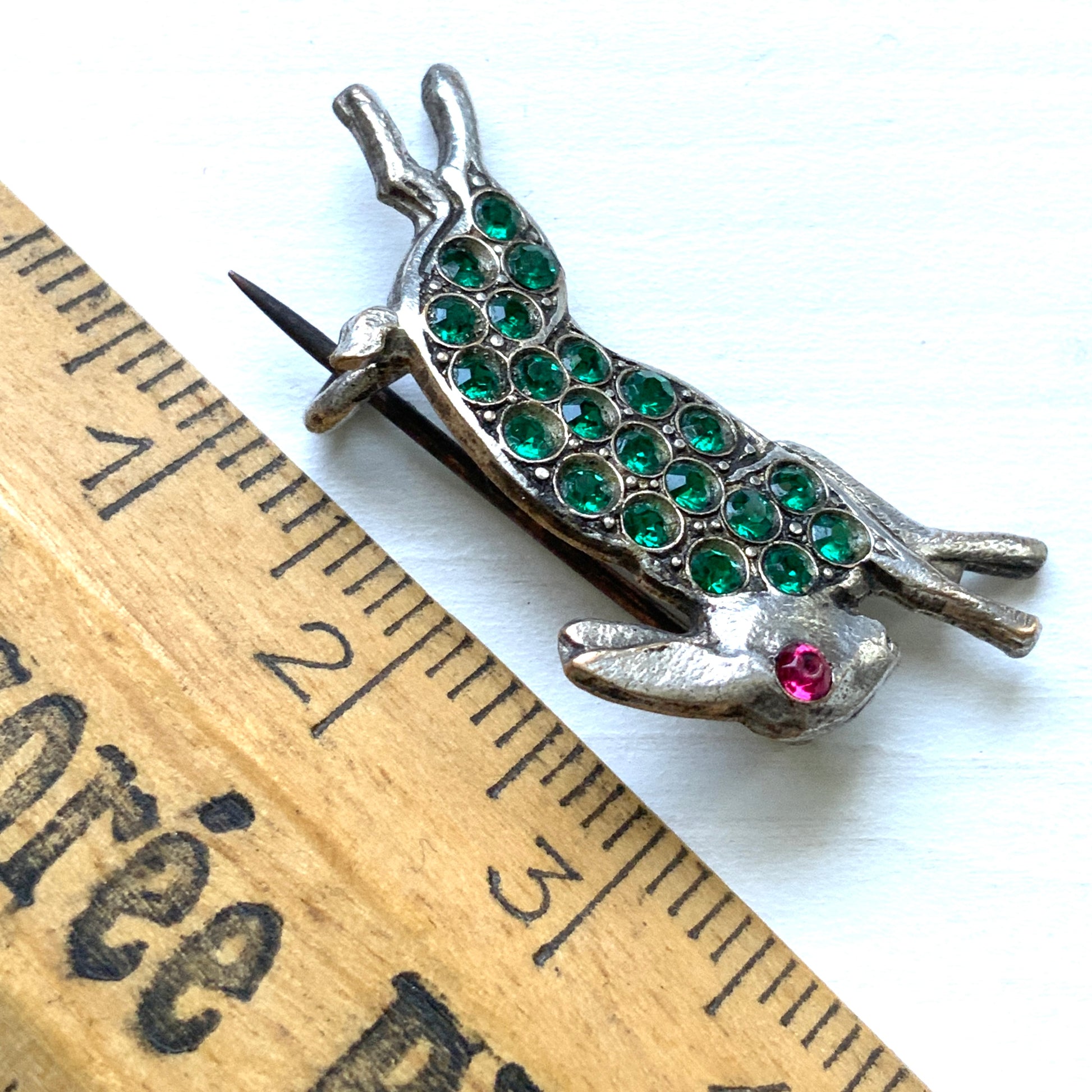 This silver brooch features a rabbit with green rhinestones adorning its body. グリーンのラインストーンをボディに纏ったうさぎのシルバーブローチ。