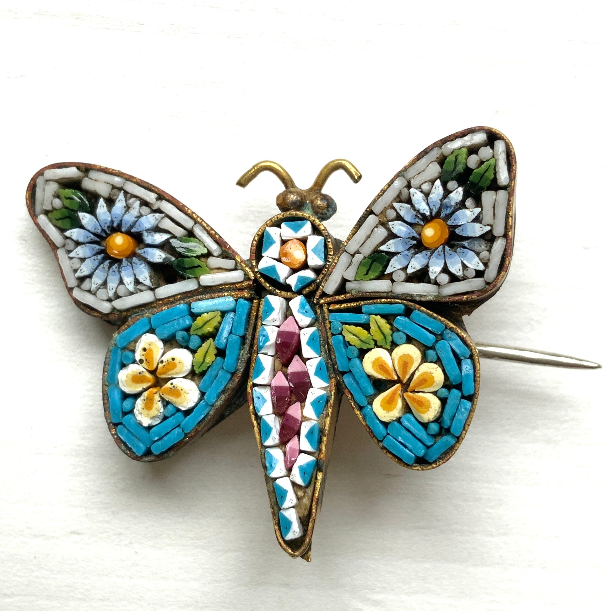 A micro mosaic butterfly brooch featuring delicate floral designs on its wings. お花が羽に入ったマイクロモザイク の蝶々のブローチ。
