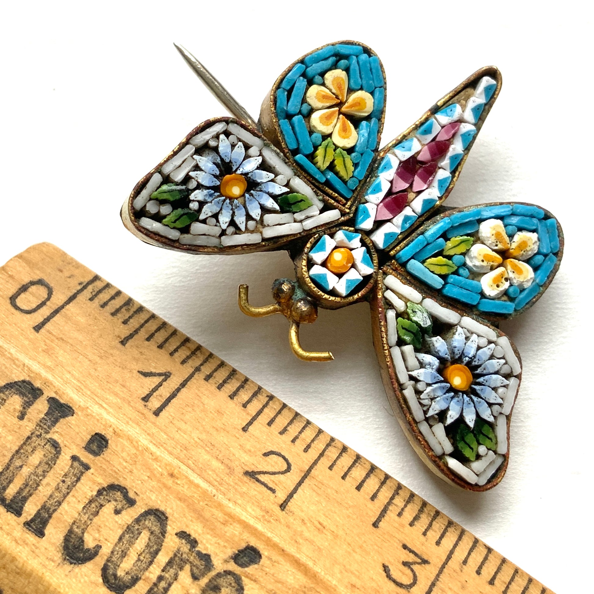 A micro mosaic butterfly brooch featuring delicate floral designs on its wings. お花が羽に入ったマイクロモザイク の蝶々のブローチ。