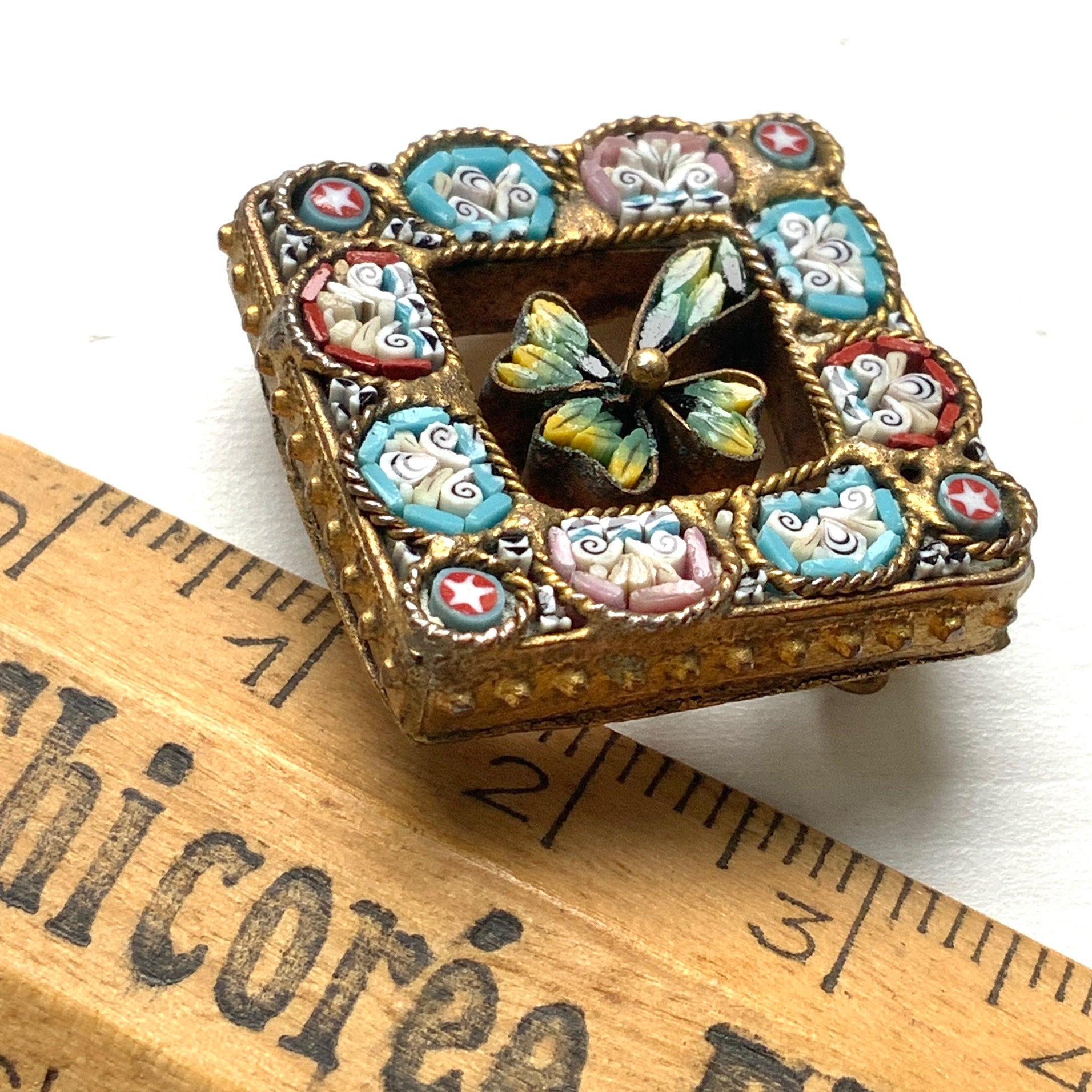 A brooch featuring a three-leaf clover set inside a diamond-shaped frame adorned with delicate detailing. 細かな飾りが飾られたダイヤ型のフレームの中に、三つ葉のクローバーが入ったブローチ。