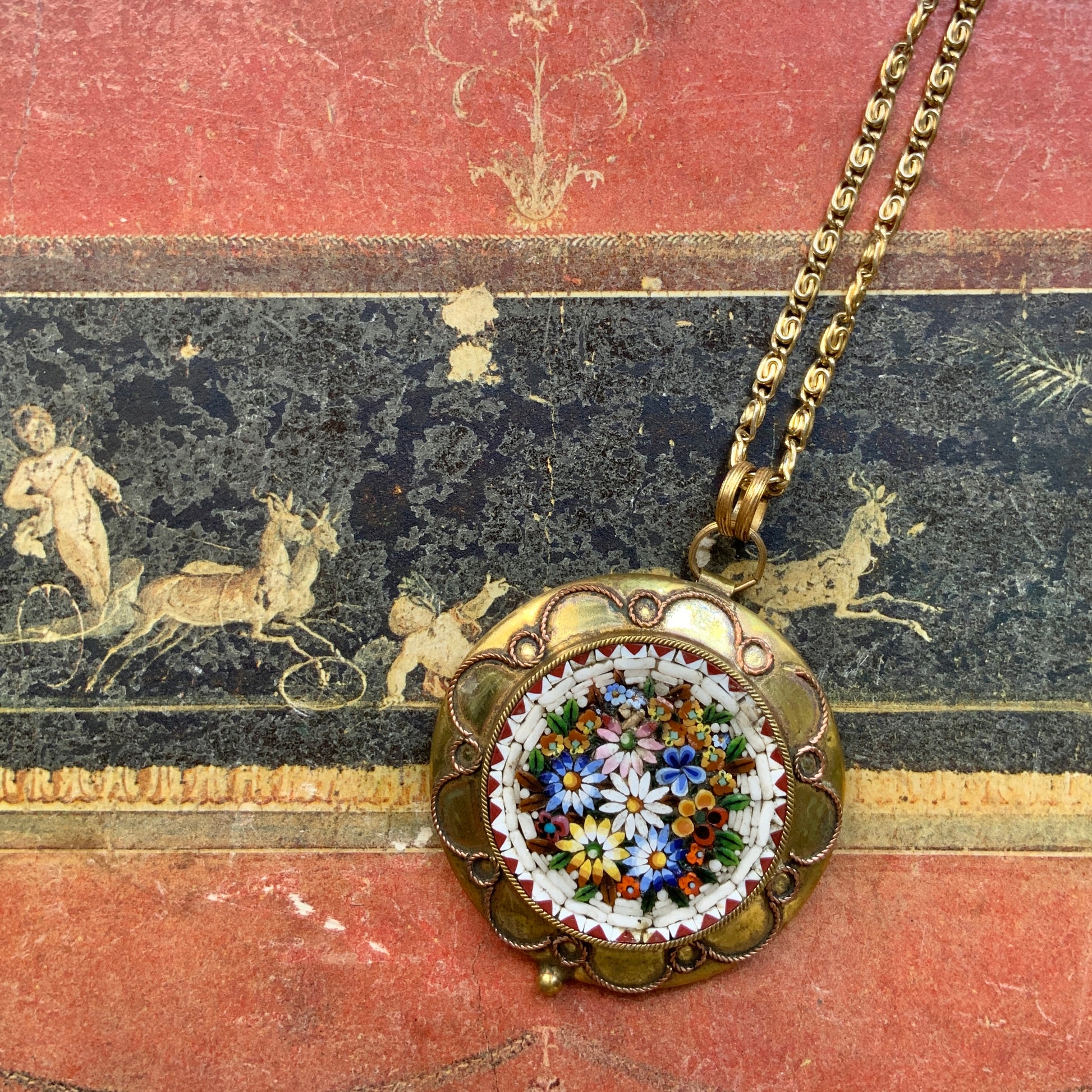 This pendant necklace features a base of gold-tone metal adorned with colorful floral micro-mosaics.  ゴールドトーンメタルをベースに、カラフルな花々のマイクロモザイクがあしらわれたペンダントネックレス。