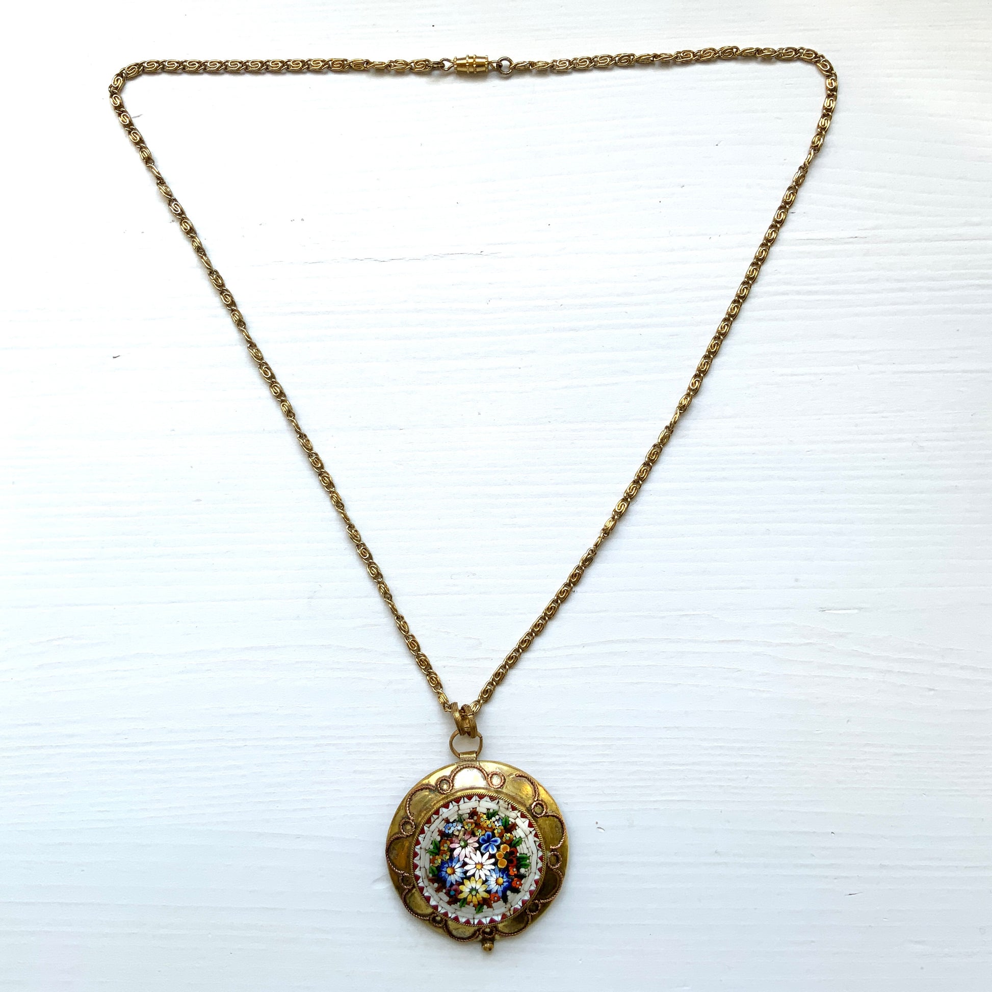 This pendant necklace features a base of gold-tone metal adorned with colorful floral micro-mosaics.  ゴールドトーンメタルをベースに、カラフルな花々のマイクロモザイクがあしらわれたペンダントネックレス。