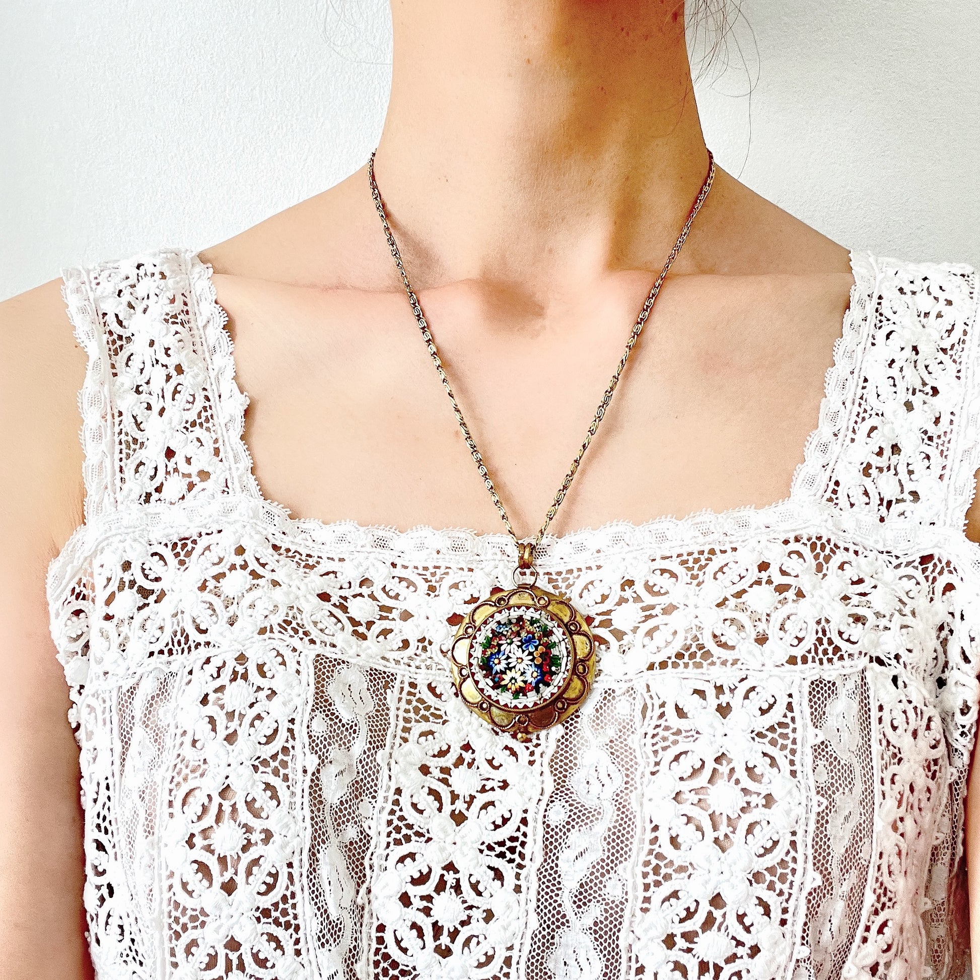 This pendant necklace features a base of gold-tone metal adorned with colorful floral micro-mosaics.  ゴールドトーンメタルをベースに、カラフルな花々のマイクロモザイクがあしらわれたペンダントネックレス。