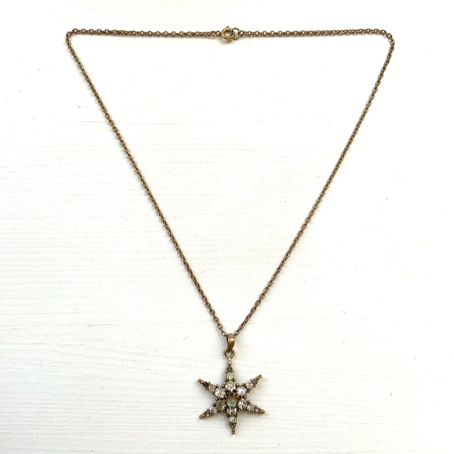 An antique pendant necklace featuring a starburst design with a mysterious glass stone known as Saphiret set in the centre. 神秘的な輝きを放つサフィレットを中央に添えた、ラインストーンのスターバーストデザインのペンダントネックレス。
