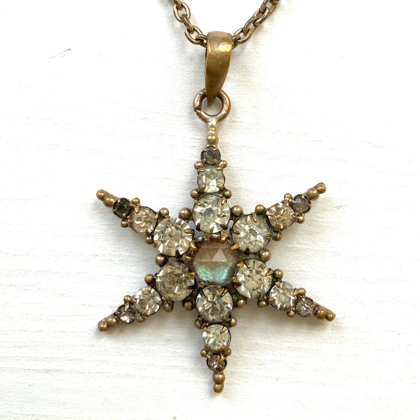 An antique pendant necklace featuring a starburst design with a mysterious glass stone known as Saphiret set in the centre. 神秘的な輝きを放つサフィレットを中央に添えた、ラインストーンのスターバーストデザインのペンダントネックレス。