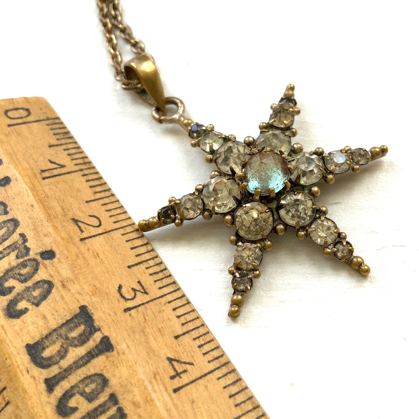 An antique pendant necklace featuring a starburst design with a mysterious glass stone known as Saphiret set in the centre. 神秘的な輝きを放つサフィレットを中央に添えた、ラインストーンのスターバーストデザインのペンダントネックレス。