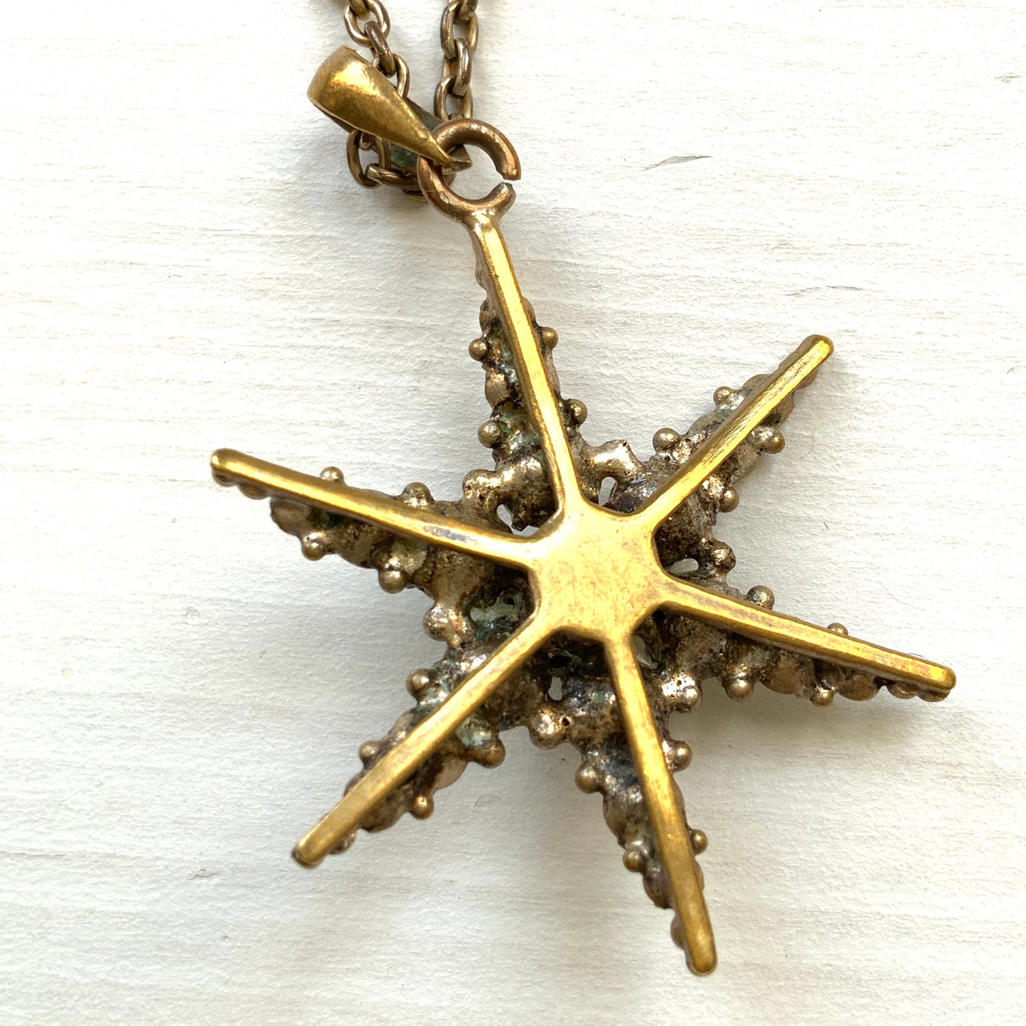 An antique pendant necklace featuring a starburst design with a mysterious glass stone known as Saphiret set in the centre. 神秘的な輝きを放つサフィレットを中央に添えた、ラインストーンのスターバーストデザインのペンダントネックレス。