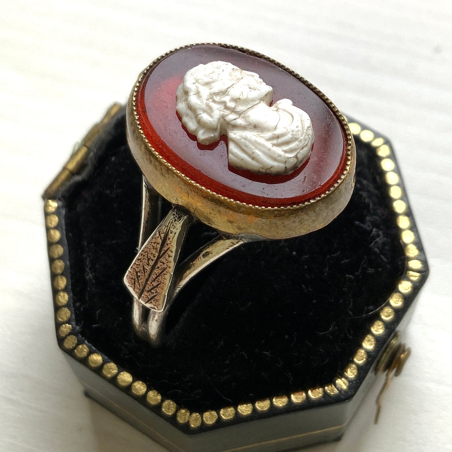 A Victorian ring with a cameo composed of a red glass base and a white porcelain overlay, imitating the look of carnelian two-layer stone. カーネリアンの二層石のカメオを、赤いガラスのベースと白い陶器のカメオで再現したヴィクトリア時代のリング。