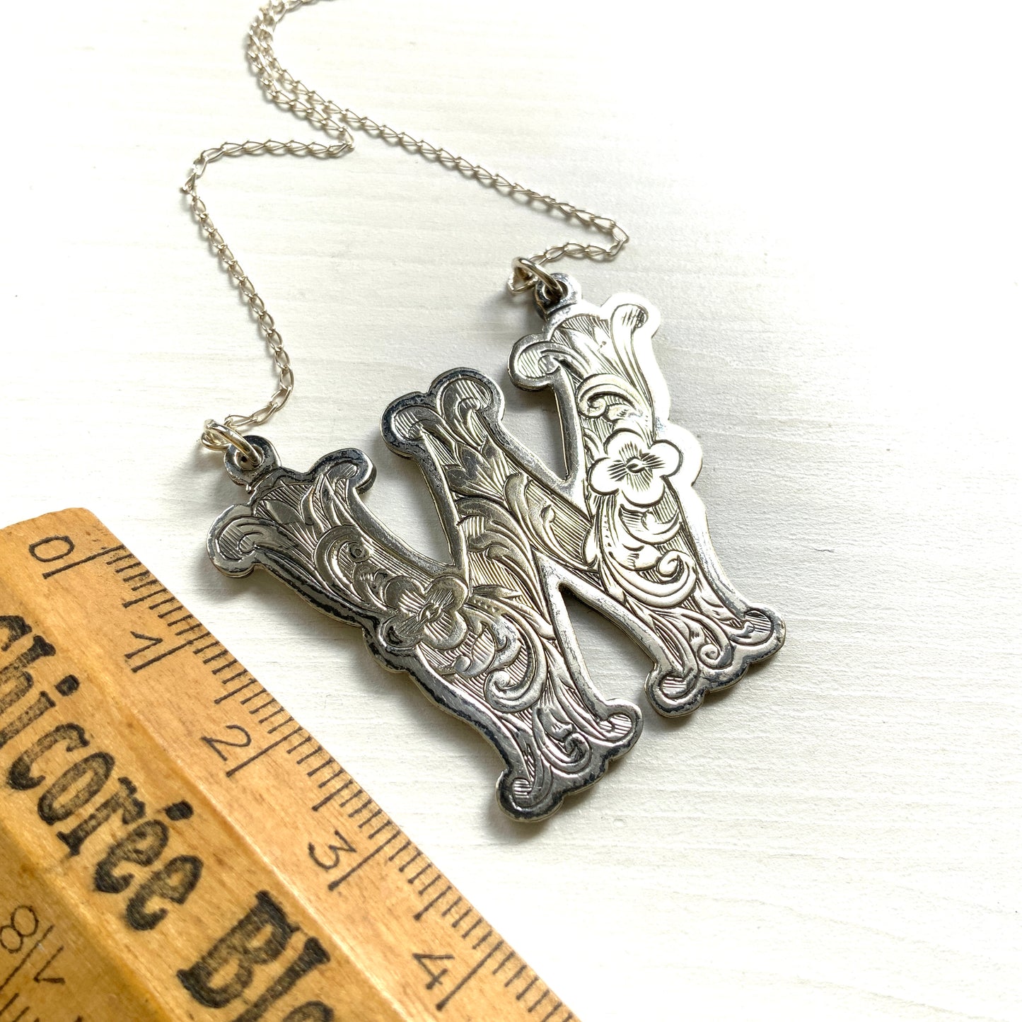 A necklace featuring the letter “W”, beautifully engraved with a botanical motif. 美しい植物モチーフのエングレービングが施された“W”のネックレス。