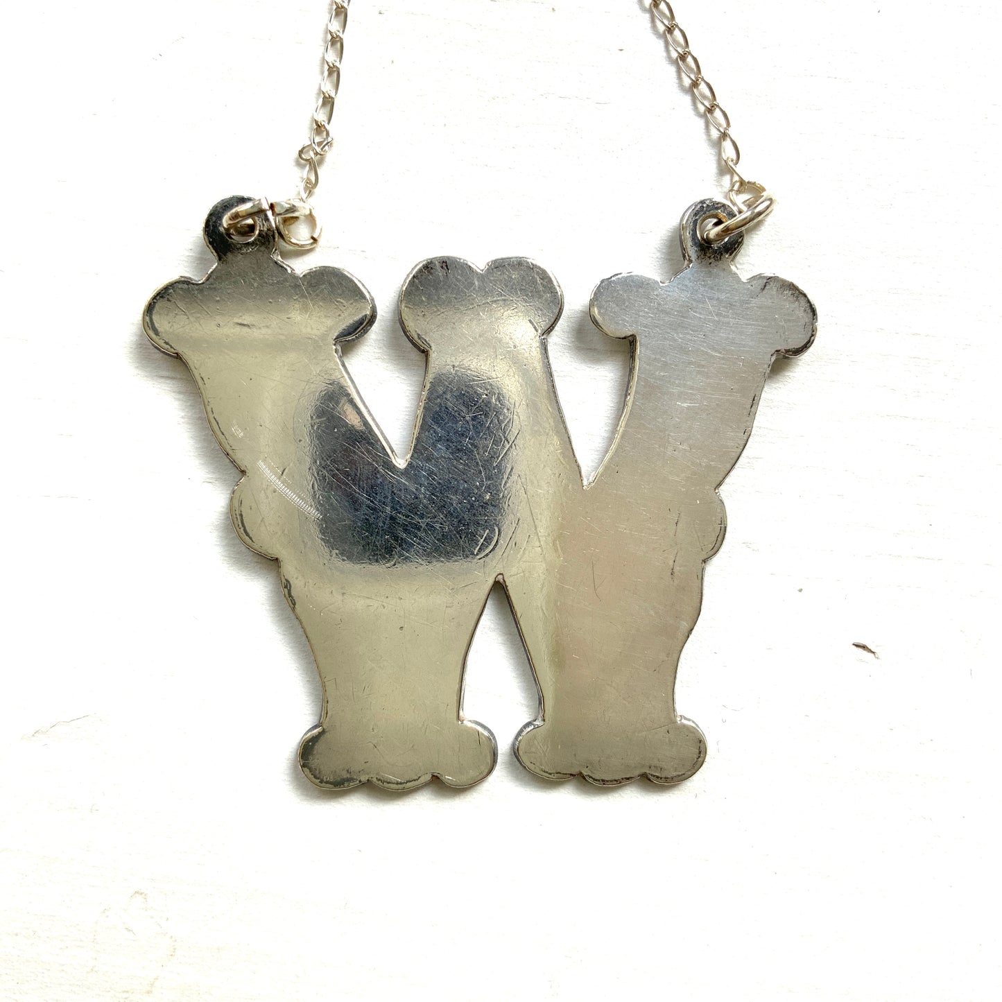 A necklace featuring the letter “W”, beautifully engraved with a botanical motif. 美しい植物モチーフのエングレービングが施された“W”のネックレス。
