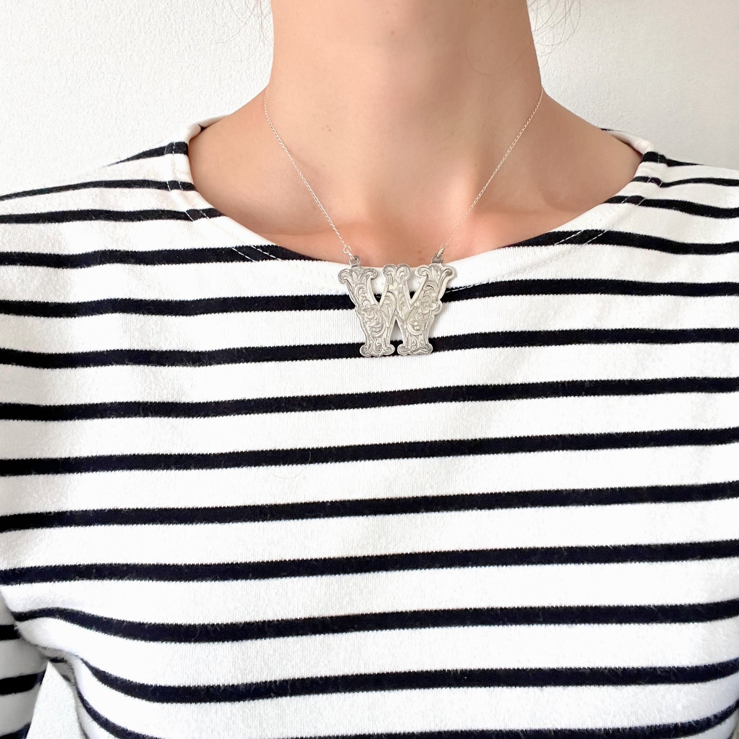 A necklace featuring the letter “W”, beautifully engraved with a botanical motif. 美しい植物モチーフのエングレービングが施された“W”のネックレス。