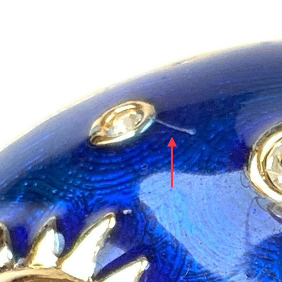 A dome-shaped brooch adorned with vibrant blue enamel, featuring silver-tone celestial motifs such as the sun face, crescent moon face, Saturn, and stars. 鮮やかなブルーのエナメルが施されたドームに、シルバートーンの太陽や三日月フェイスや、土星や星などが浮かんだブローチ。
