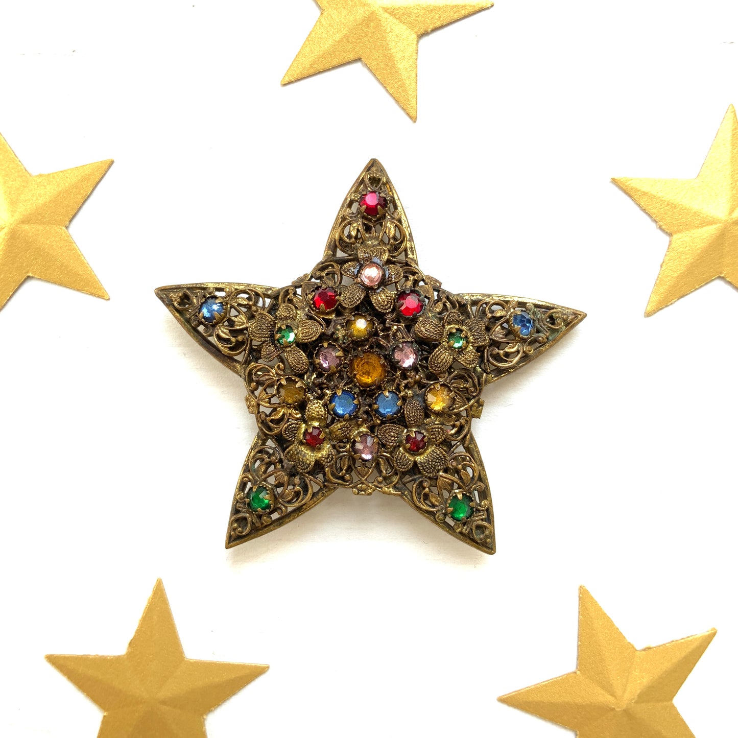 A beautiful vintage brooch featuring a star-shaped design crafted in intricate gold-tone filigree, adorned with multicoloured rhinestones. ゴールドトーンの繊細なフィリグリー細工でかたどられた星に、色とりどりのラインストーンがあしらわれたヴィンテージブローチ。