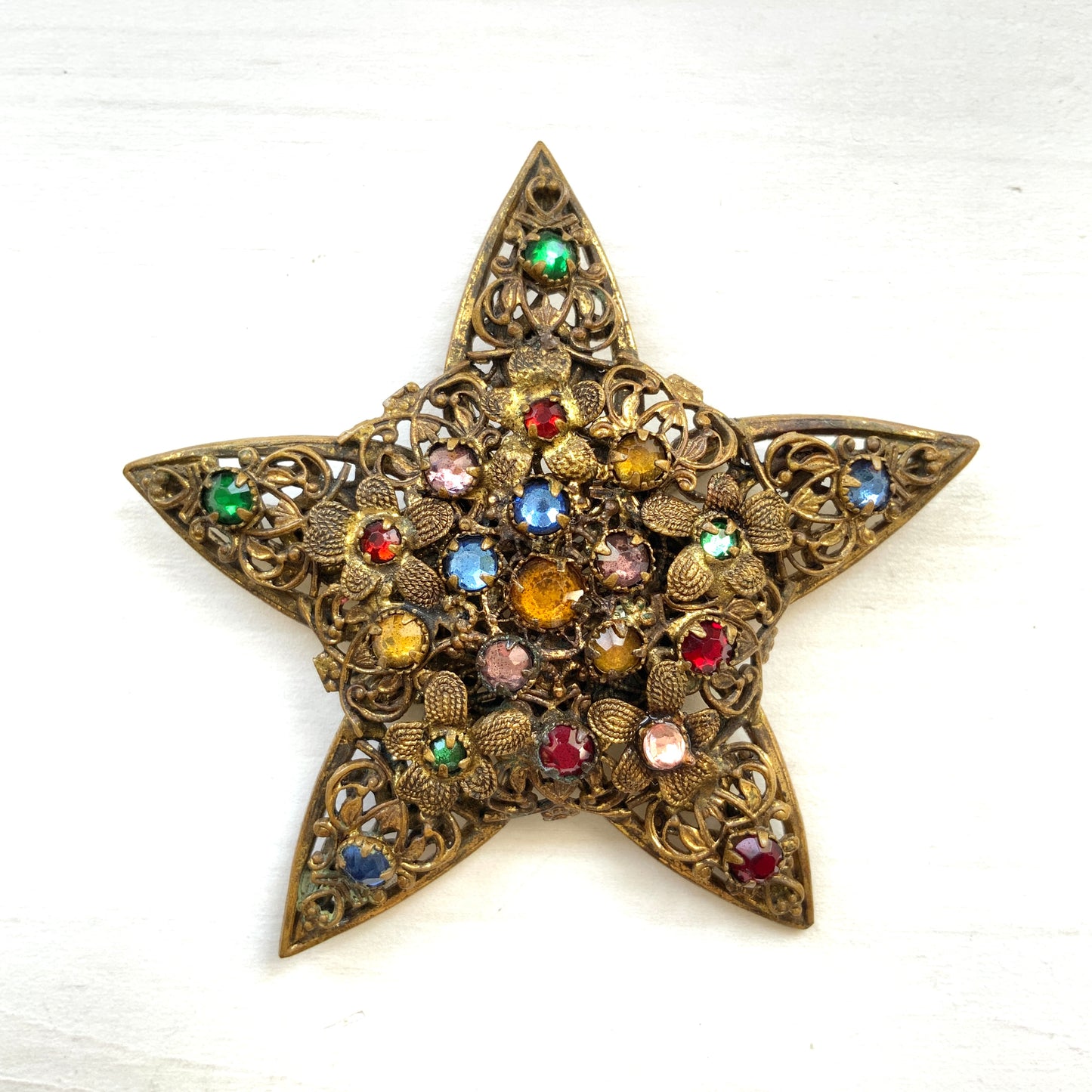 A beautiful vintage brooch featuring a star-shaped design crafted in intricate gold-tone filigree, adorned with multicoloured rhinestones. ゴールドトーンの繊細なフィリグリー細工でかたどられた星に、色とりどりのラインストーンがあしらわれたヴィンテージブローチ。