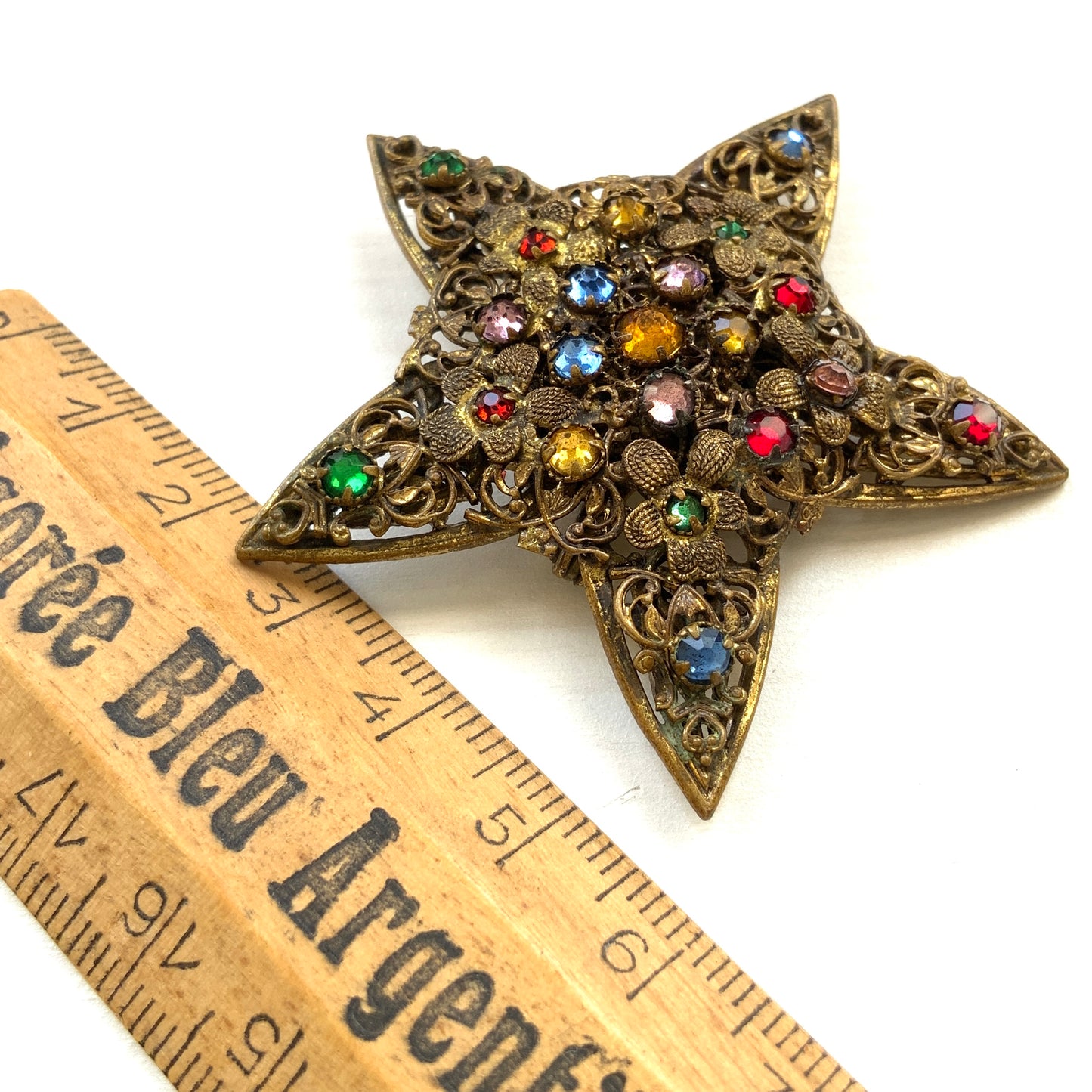 A beautiful vintage brooch featuring a star-shaped design crafted in intricate gold-tone filigree, adorned with multicoloured rhinestones. ゴールドトーンの繊細なフィリグリー細工でかたどられた星に、色とりどりのラインストーンがあしらわれたヴィンテージブローチ。