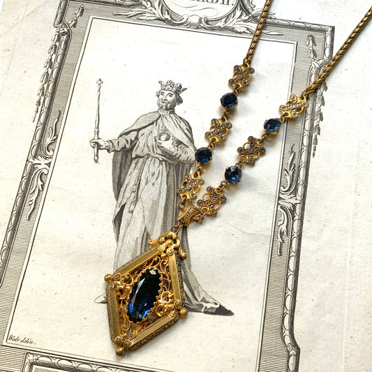 This necklace features a deep ocean-blue oval glass stone set at the center of a beautifully decorated diamond-shaped plate. 深い海のようなディープブルーのオーバルグラスが、美しい装飾を施したダイヤ型プレートの中央にあしらわれたネックレスです。