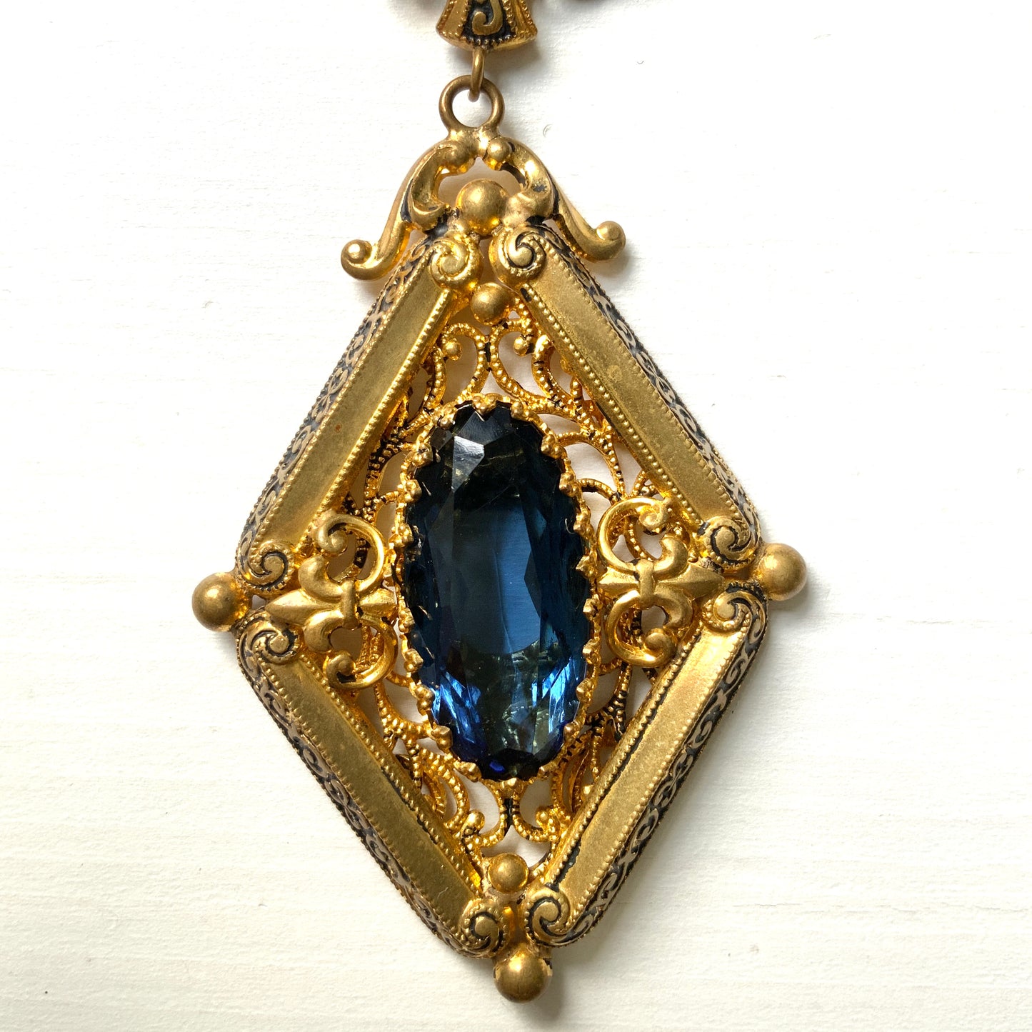 This necklace features a deep ocean-blue oval glass stone set at the center of a beautifully decorated diamond-shaped plate. 深い海のようなディープブルーのオーバルグラスが、美しい装飾を施したダイヤ型プレートの中央にあしらわれたネックレスです。