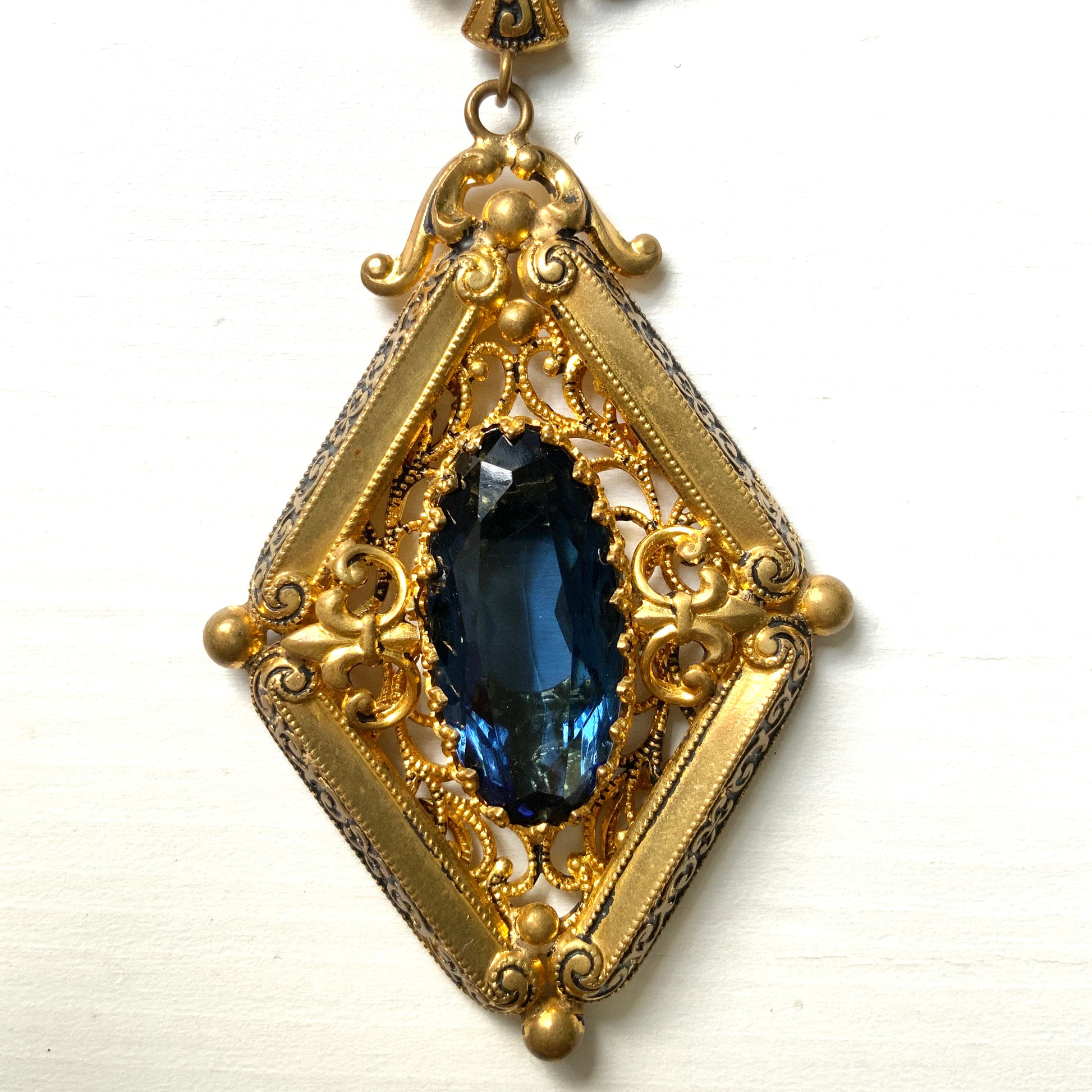 This necklace features a deep ocean-blue oval glass stone set at the center of a beautifully decorated diamond-shaped plate. 深い海のようなディープブルーのオーバルグラスが、美しい装飾を施したダイヤ型プレートの中央にあしらわれたネックレスです。