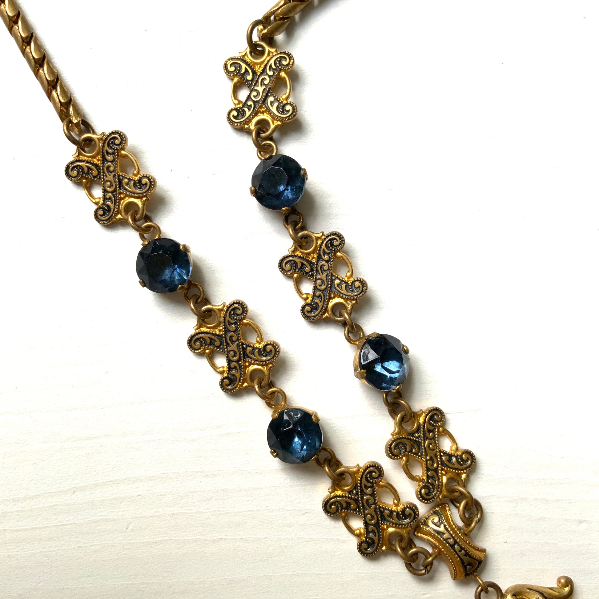 This necklace features a deep ocean-blue oval glass stone set at the center of a beautifully decorated diamond-shaped plate. 深い海のようなディープブルーのオーバルグラスが、美しい装飾を施したダイヤ型プレートの中央にあしらわれたネックレスです。