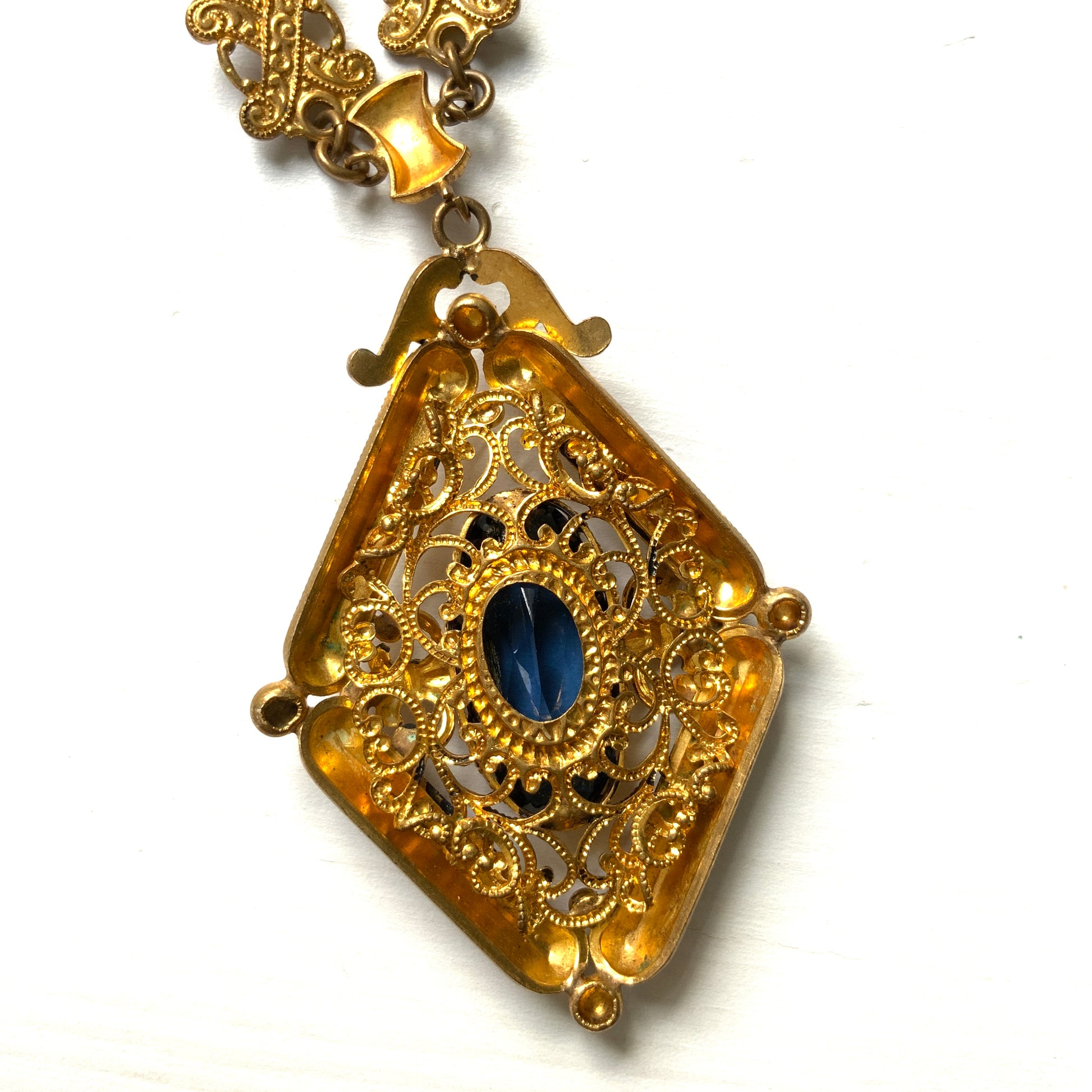 This necklace features a deep ocean-blue oval glass stone set at the center of a beautifully decorated diamond-shaped plate. 深い海のようなディープブルーのオーバルグラスが、美しい装飾を施したダイヤ型プレートの中央にあしらわれたネックレスです。