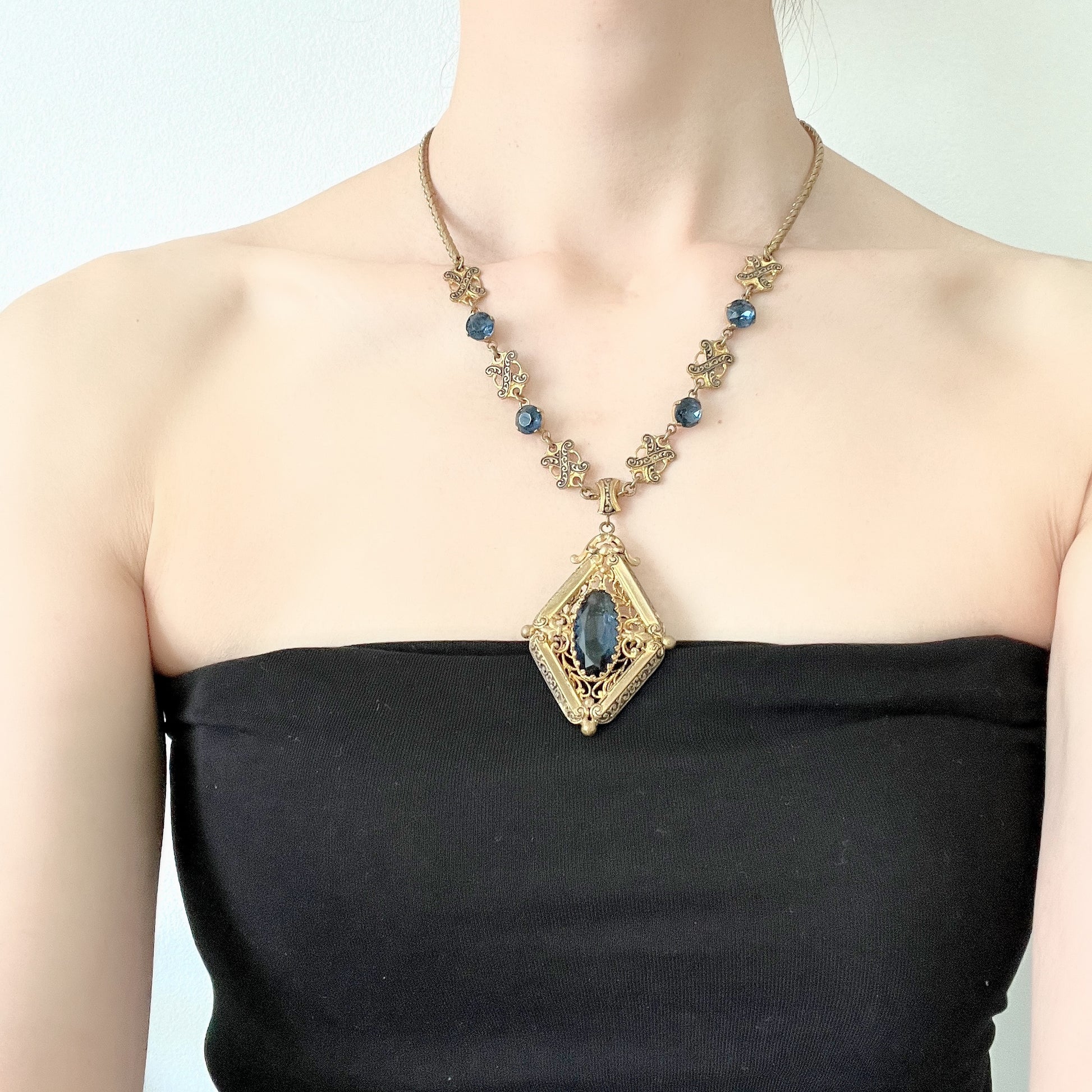 This necklace features a deep ocean-blue oval glass stone set at the center of a beautifully decorated diamond-shaped plate. 深い海のようなディープブルーのオーバルグラスが、美しい装飾を施したダイヤ型プレートの中央にあしらわれたネックレスです。
