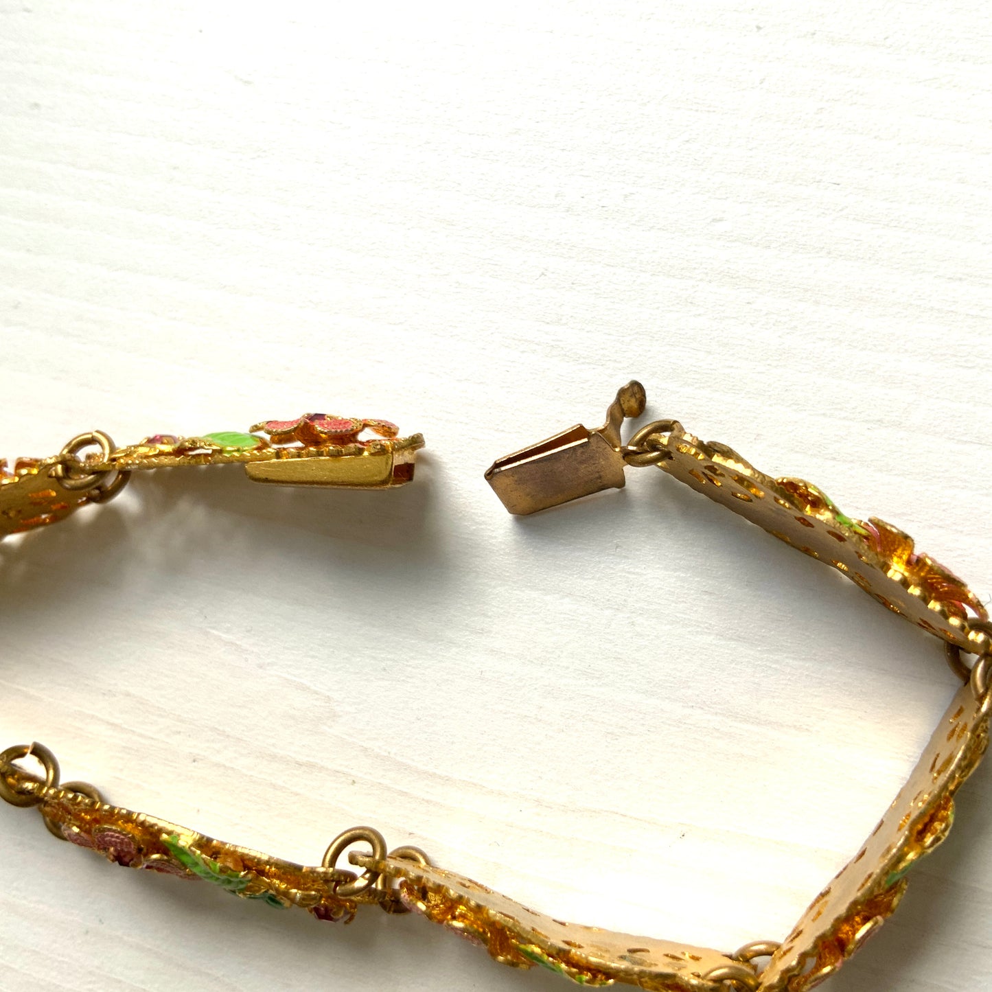 This gold-tone filigree bracelet features charming pink flowers delicately painted onto its dainty filigree plates. かわいらしいピンクのお花が描かれたゴールドトーンのフィリグリーのブレスレット。