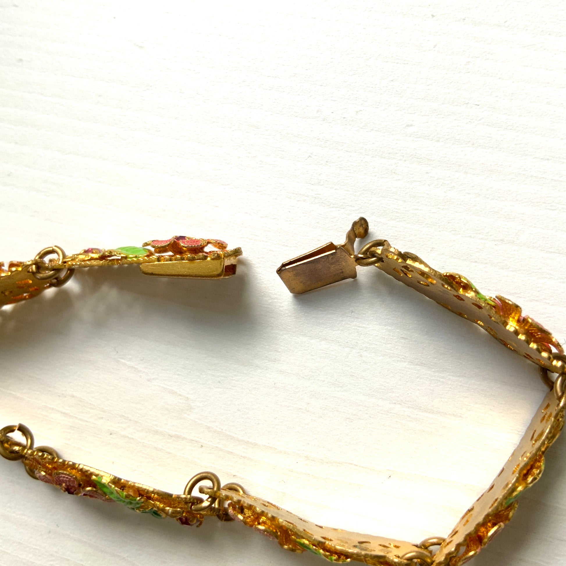 This gold-tone filigree bracelet features charming pink flowers delicately painted onto its dainty filigree plates. かわいらしいピンクのお花が描かれたゴールドトーンのフィリグリーのブレスレット。