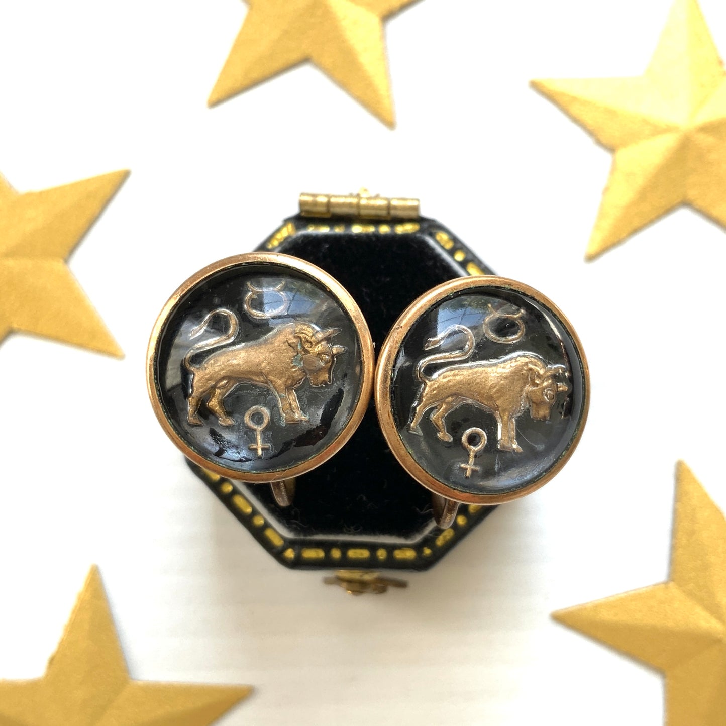 Screw-back earrings featuring an reverse carved design of a Taurus bull . 黒地にゴールドトーンで牡牛とそのシンボルが裏彫りされた、ヴィンテージのスクリューイヤリング。