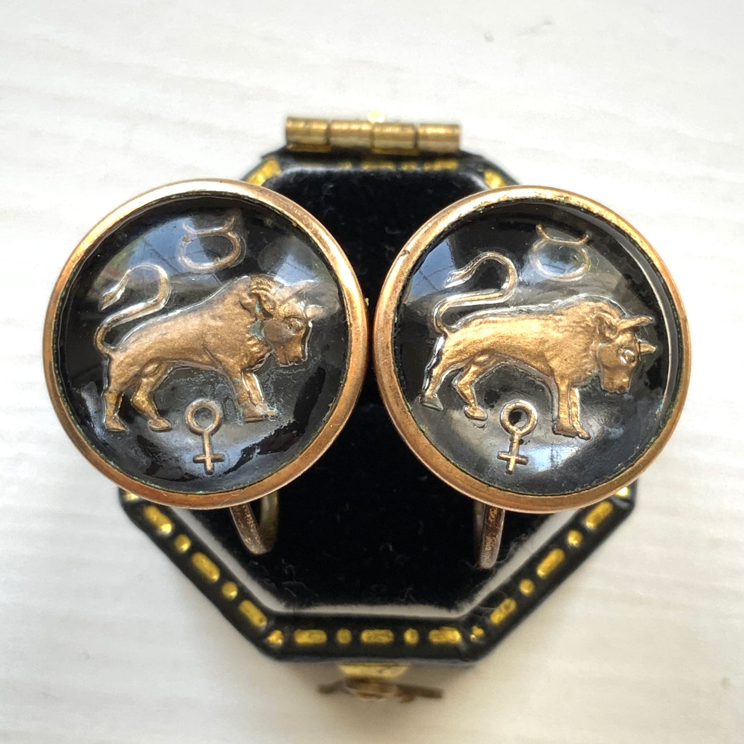 Screw-back earrings featuring an reverse carved design of a Taurus bull . 黒地にゴールドトーンで牡牛とそのシンボルが裏彫りされた、ヴィンテージのスクリューイヤリング。
