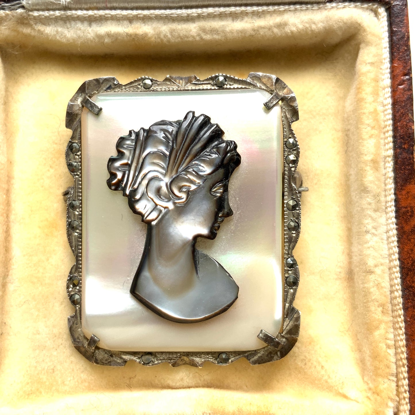 A brooch featuring a cameo of a lady’s profile carved in black mother of pearl, set against a white mother of pearl base. 白蝶貝をベースに、黒蝶貝で女性の横顔カメオをあしらったブローチ。