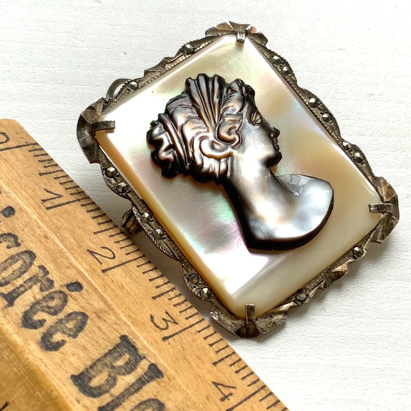 A brooch featuring a cameo of a lady’s profile carved in black mother of pearl, set against a white mother of pearl base. 白蝶貝をベースに、黒蝶貝で女性の横顔カメオをあしらったブローチ。