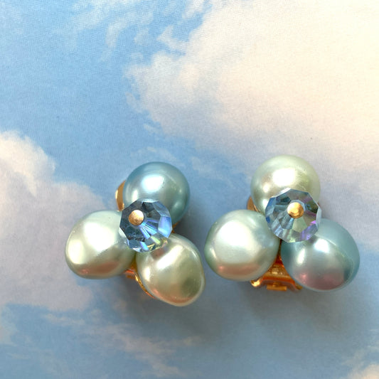 Clip-on earrings featuring three faux pearls in varying shades of blue, accented with a sparkling blue crystal bead at the center.3つの違うシェイドのブルーカラーパールがついたクリップイヤリング。