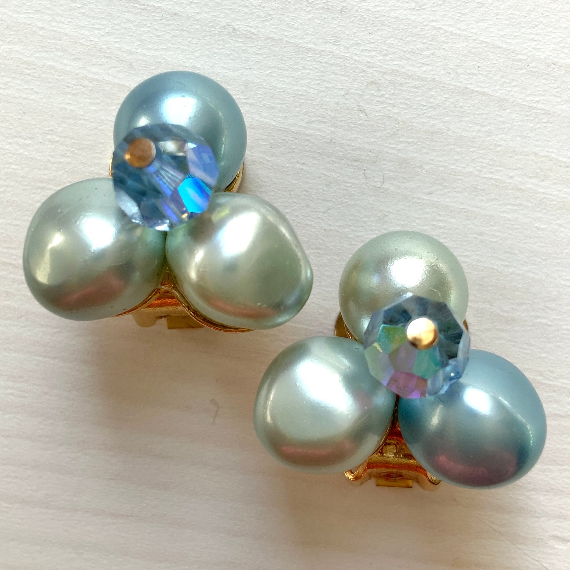 Clip-on earrings featuring three faux pearls in varying shades of blue, accented with a sparkling blue crystal bead at the center.3つの違うシェイドのブルーカラーパールがついたクリップイヤリング。