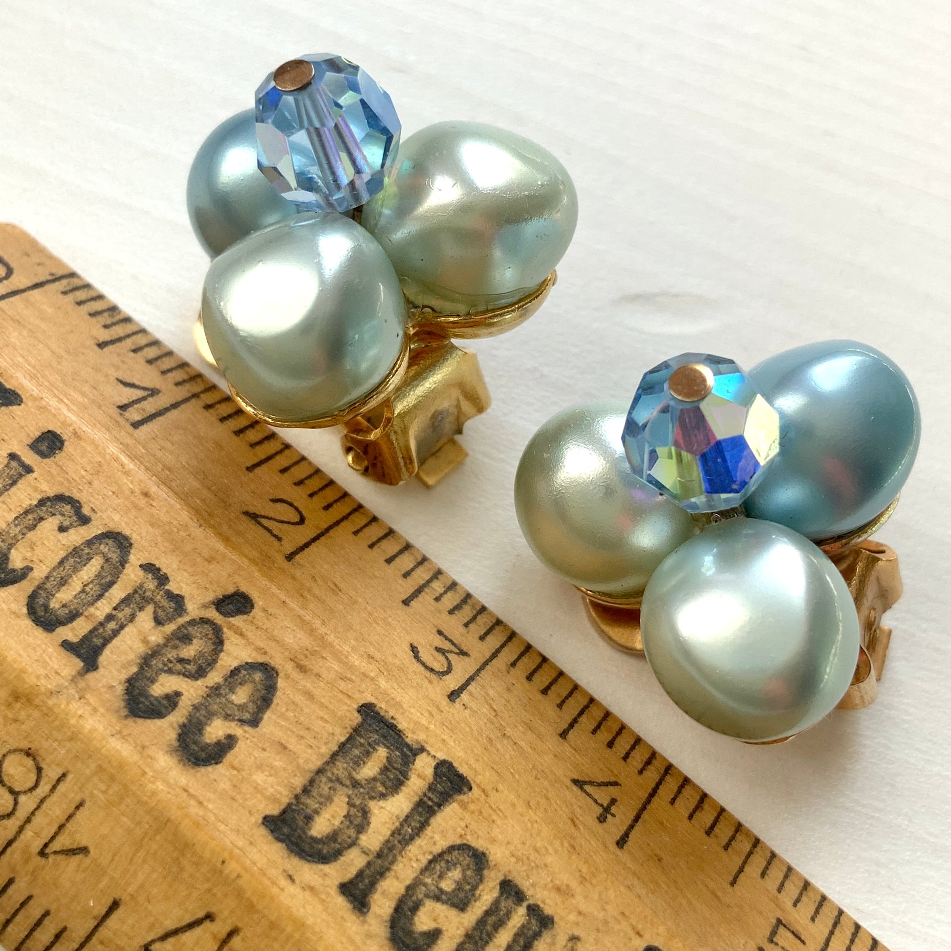 Clip-on earrings featuring three faux pearls in varying shades of blue, accented with a sparkling blue crystal bead at the center.3つの違うシェイドのブルーカラーパールがついたクリップイヤリング。