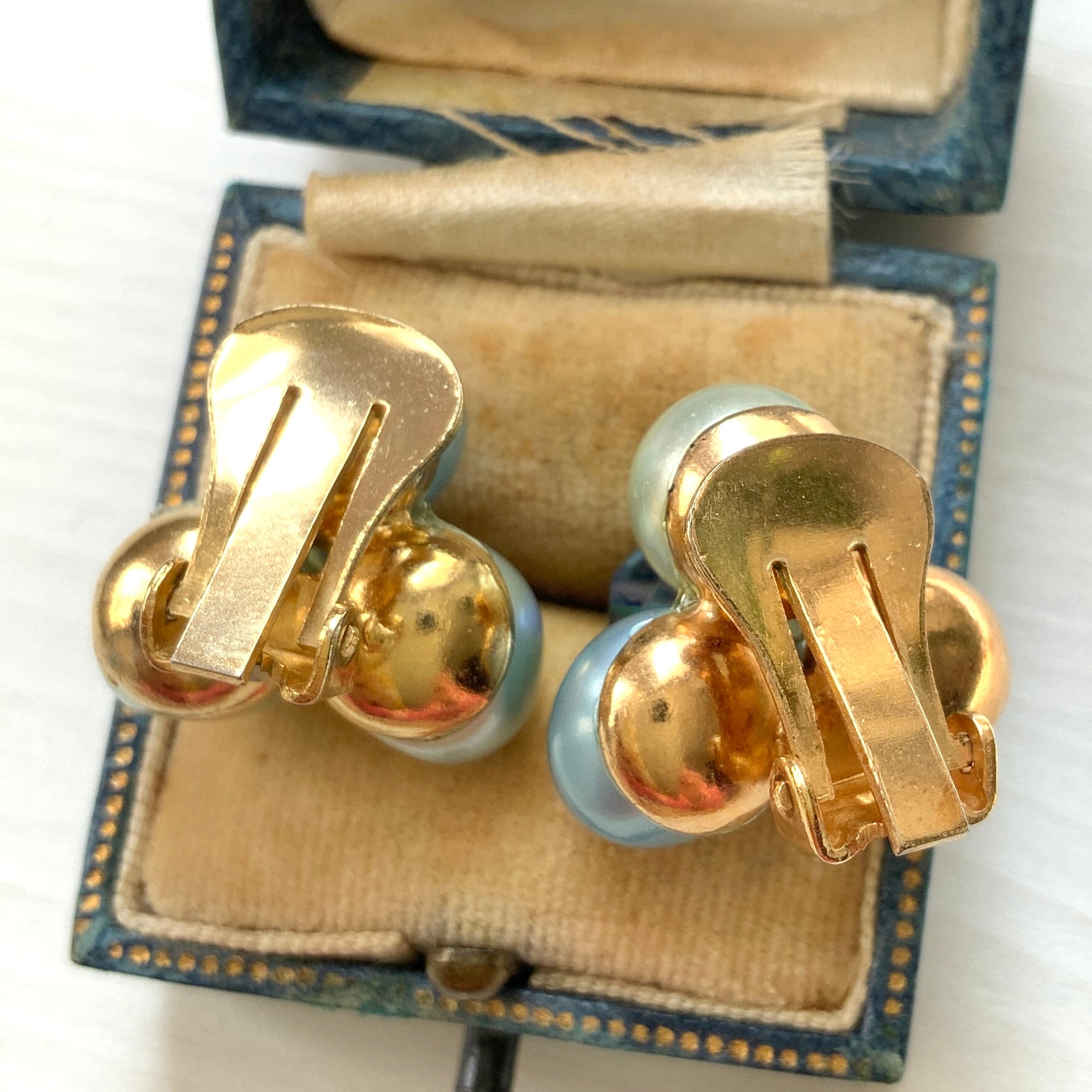 Clip-on earrings featuring three faux pearls in varying shades of blue, accented with a sparkling blue crystal bead at the center.3つの違うシェイドのブルーカラーパールがついたクリップイヤリング。
