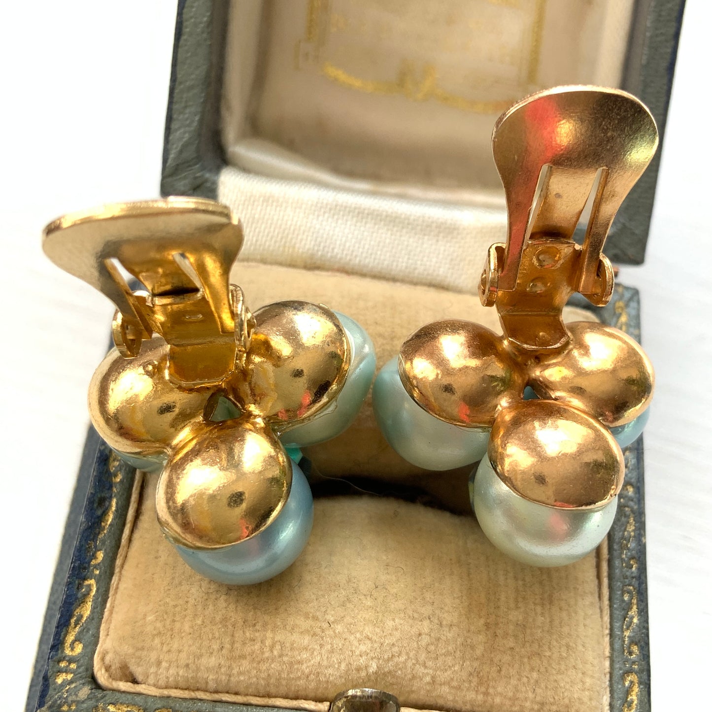 Clip-on earrings featuring three faux pearls in varying shades of blue, accented with a sparkling blue crystal bead at the center.3つの違うシェイドのブルーカラーパールがついたクリップイヤリング。