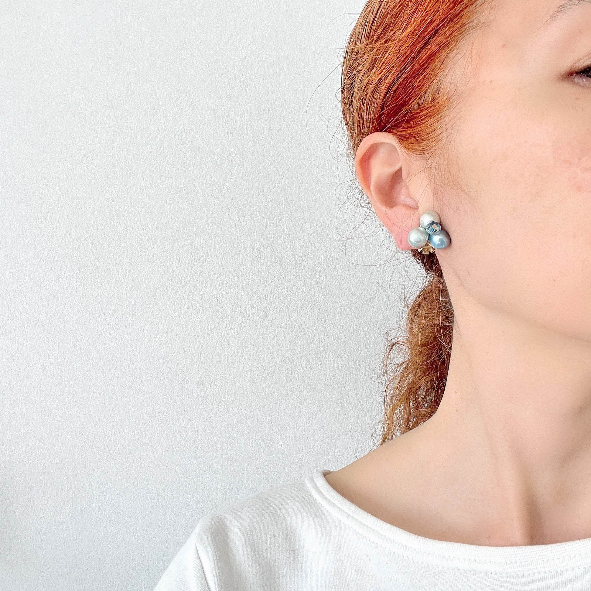 Clip-on earrings featuring three faux pearls in varying shades of blue, accented with a sparkling blue crystal bead at the center.3つの違うシェイドのブルーカラーパールがついたクリップイヤリング。