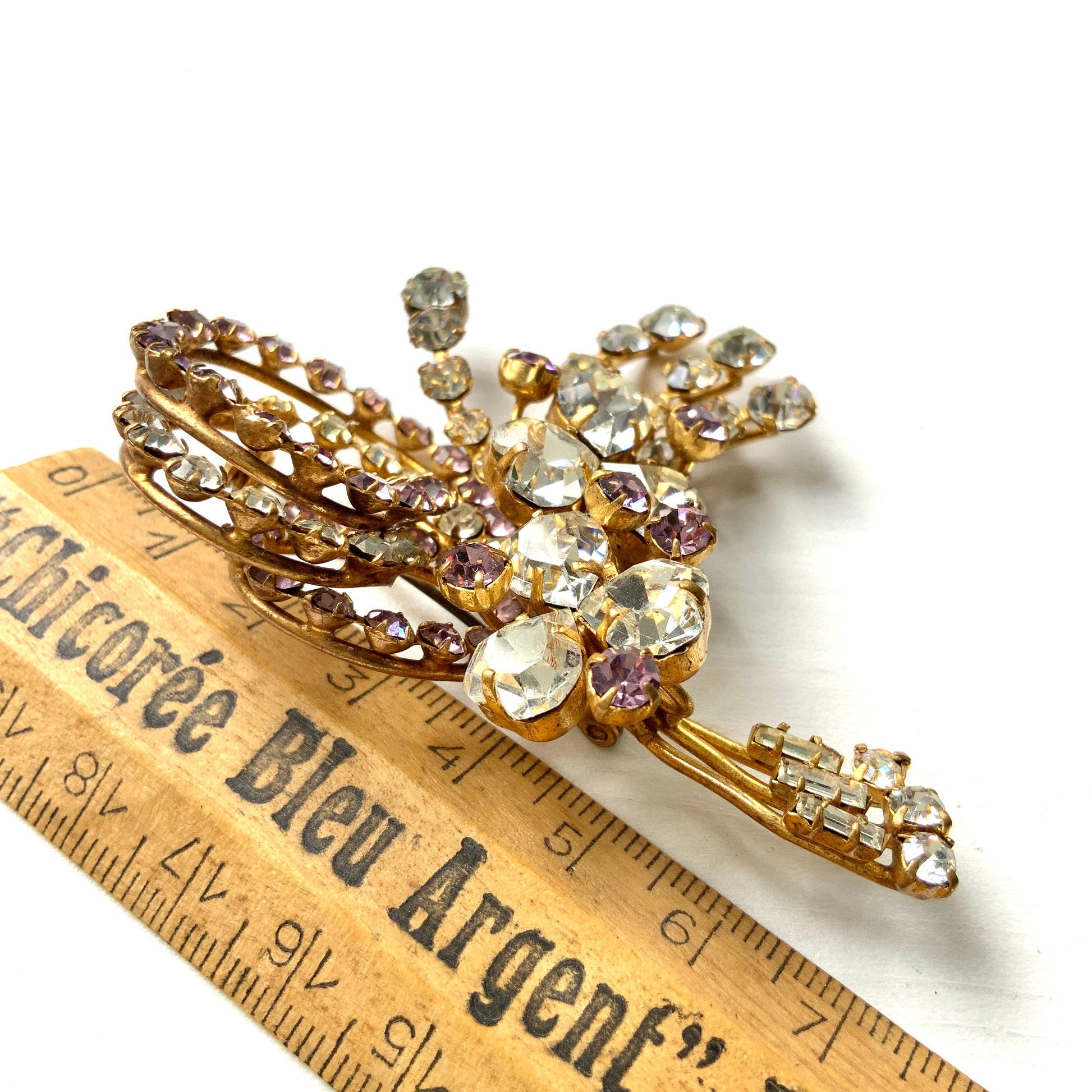 A gorgeous brooch featuring clear and lilac-colored rhinestones.  クリアカラーとライラックカラーのラインストーンのゴージャスなブローチ。