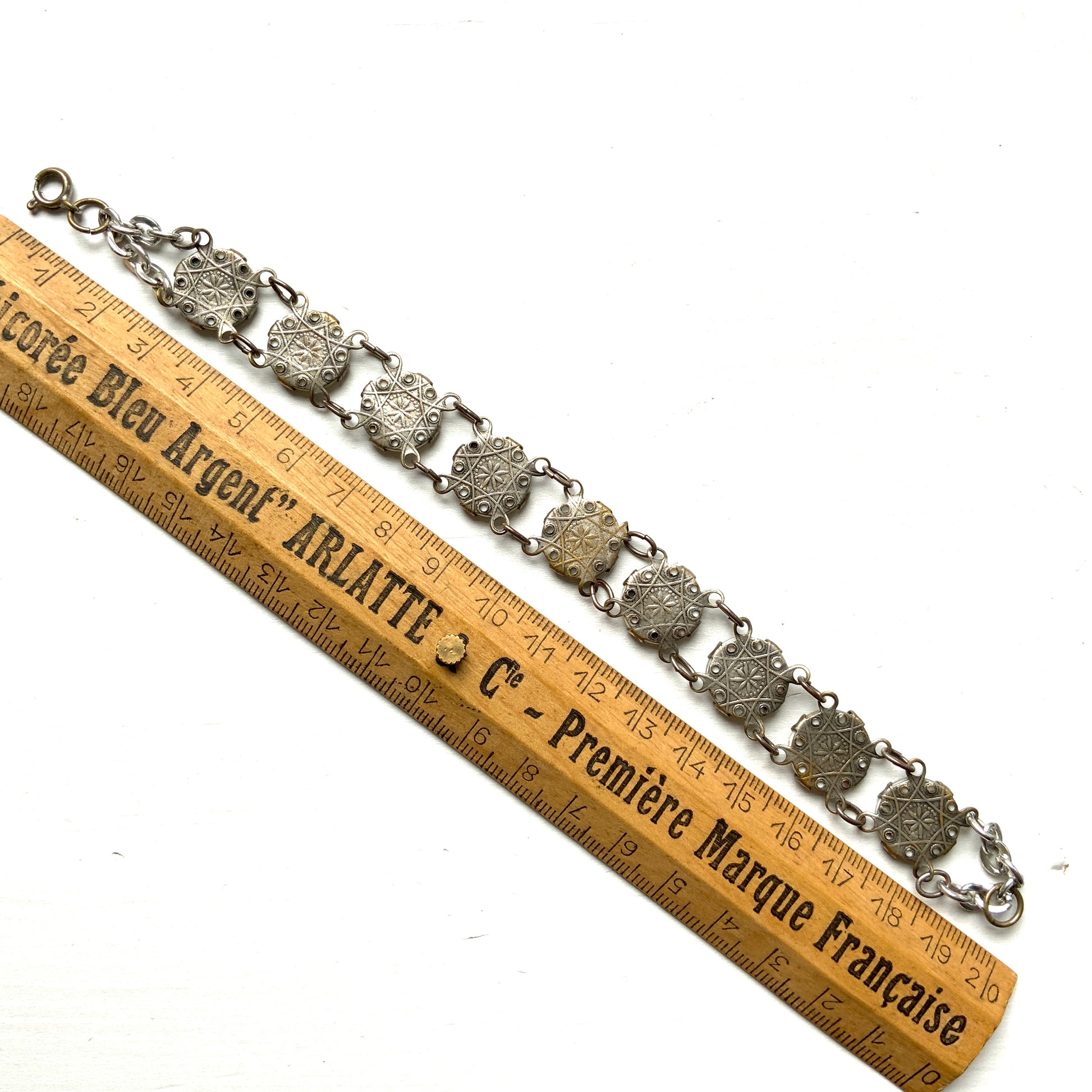 A bracelet featuring a mother of pearl tablet with the word "PARIS" and silver-tone charms of iconic Paris landmarks. マザーオブパールのタブレットに、PARISの文字とパリの観光名所のチャームがのったブレスレット。
