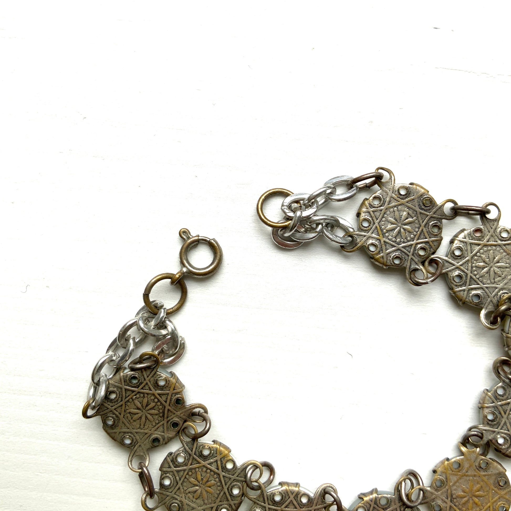 A bracelet featuring a mother of pearl tablet with the word "PARIS" and silver-tone charms of iconic Paris landmarks. マザーオブパールのタブレットに、PARISの文字とパリの観光名所のチャームがのったブレスレット。