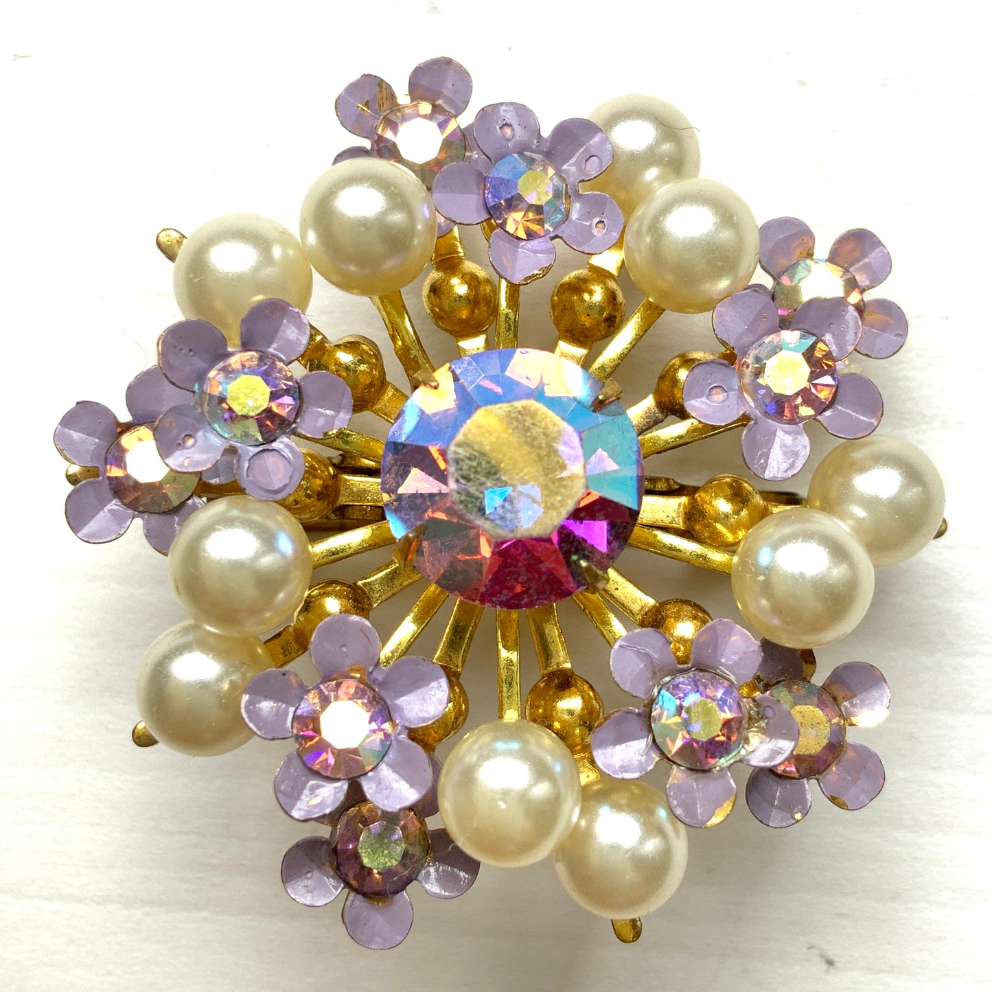 A brooch centered around large lilac-colored aurora borealis, adorned with small lilac enamel flowers and glass pearls. 大粒のライラックカラーのオーロラストーンを中心に、ライラックカラーのエナメルの小花とグラスパールがあしらわれたブローチ。